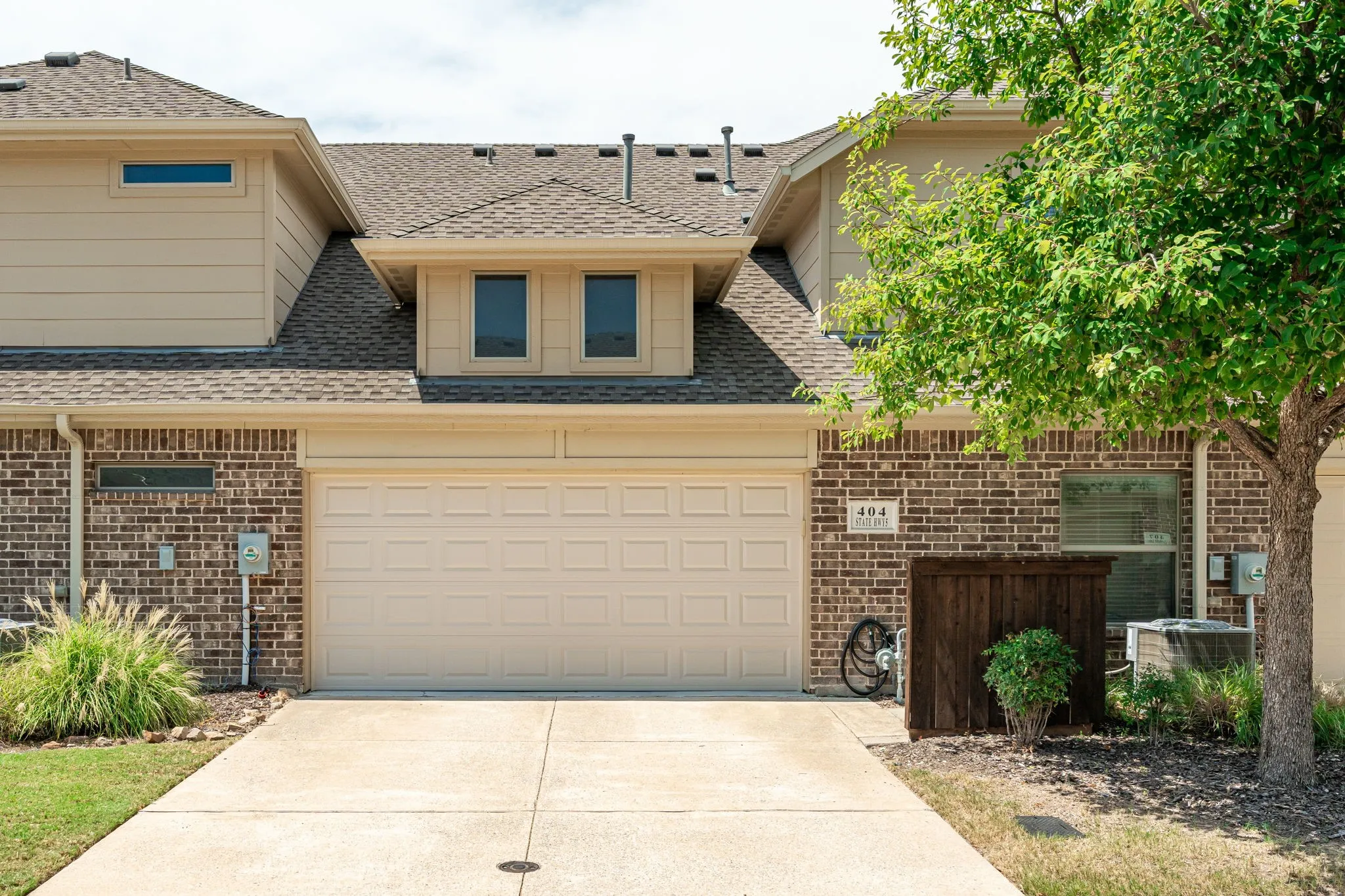 Brick and siding exterior with a concrete driveway, attached garage, dormer windows, and a shingled roof