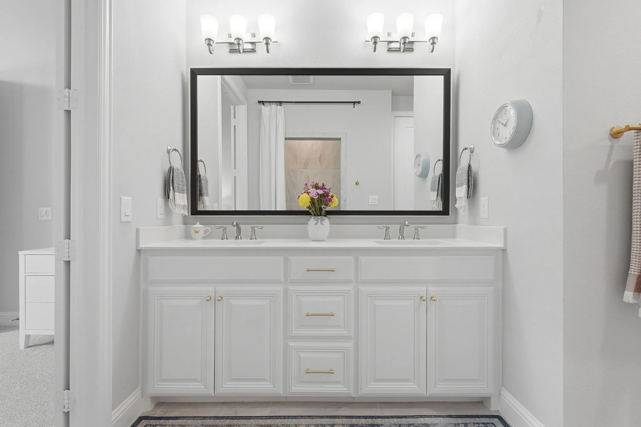 Dual vanity with white cabinetry, gold-finish hardware, and a framed mirror