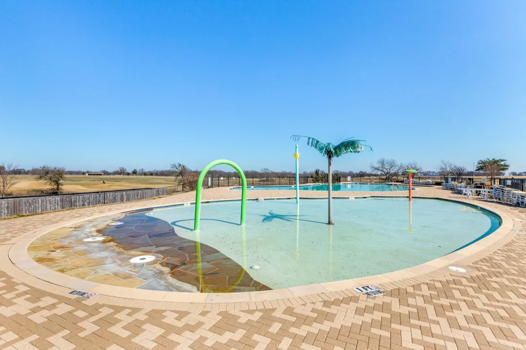 Community splash pad with multiple water features, adjacent to a large swimming pool