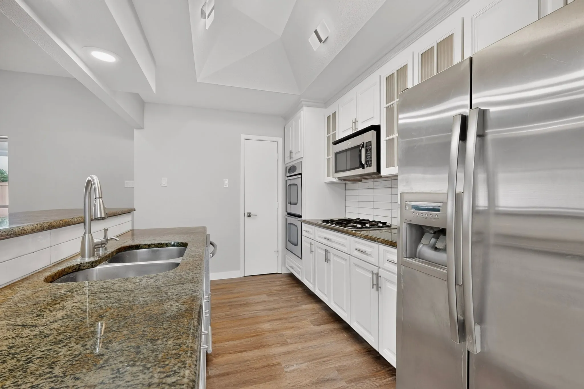 Kitchen featuring wood-finish flooring, white cabinetry, a stainless steel refrigerator, a double basin sink with a gooseneck faucet, and stone countertops
