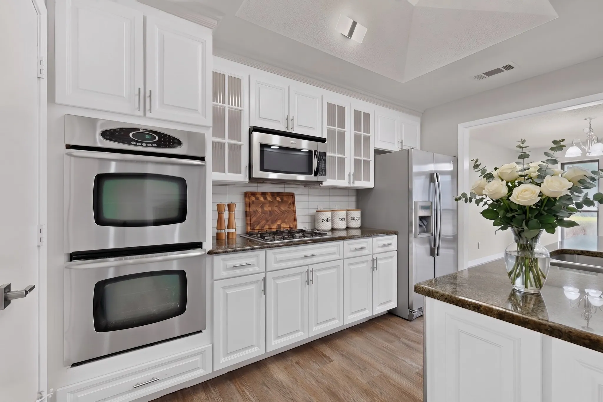 White shaker cabinetry, stainless steel double ovens, stainless steel microwave, stainless steel refrigerator, and wood-finish flooring