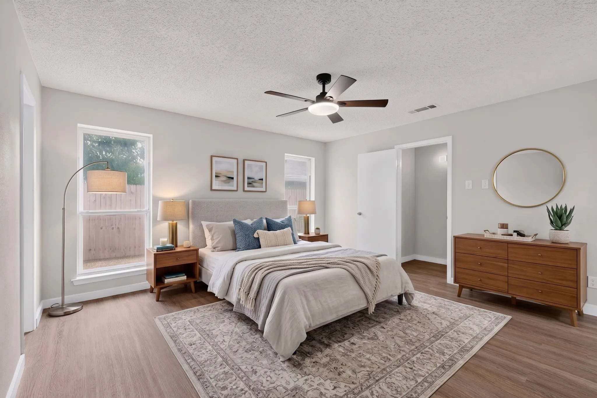 Bright interior with wood-finish flooring, two large windows, and a ceiling fan with integrated lighting
