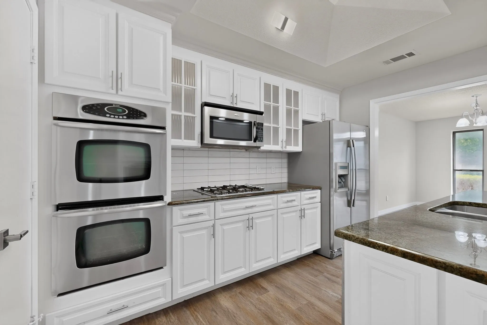 White cabinetry, stainless steel appliances, dark stone countertops, wood-finish flooring, and a white subway tile backsplash