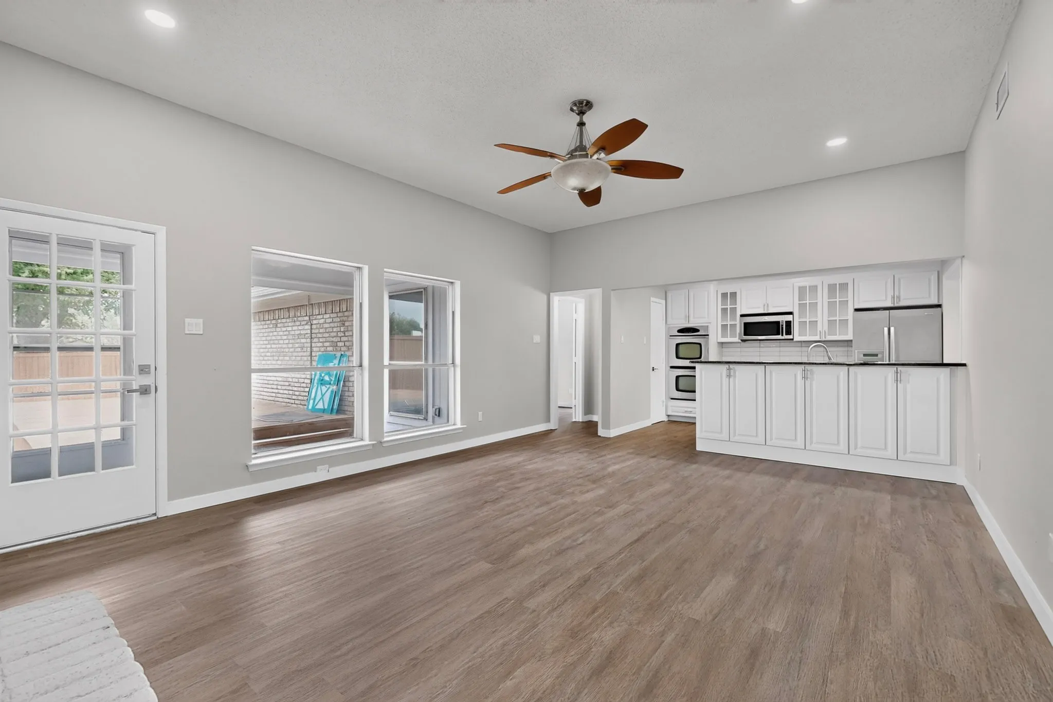 Vaulted ceiling, wood-finish flooring, white cabinetry, dark countertops, and stainless steel appliances