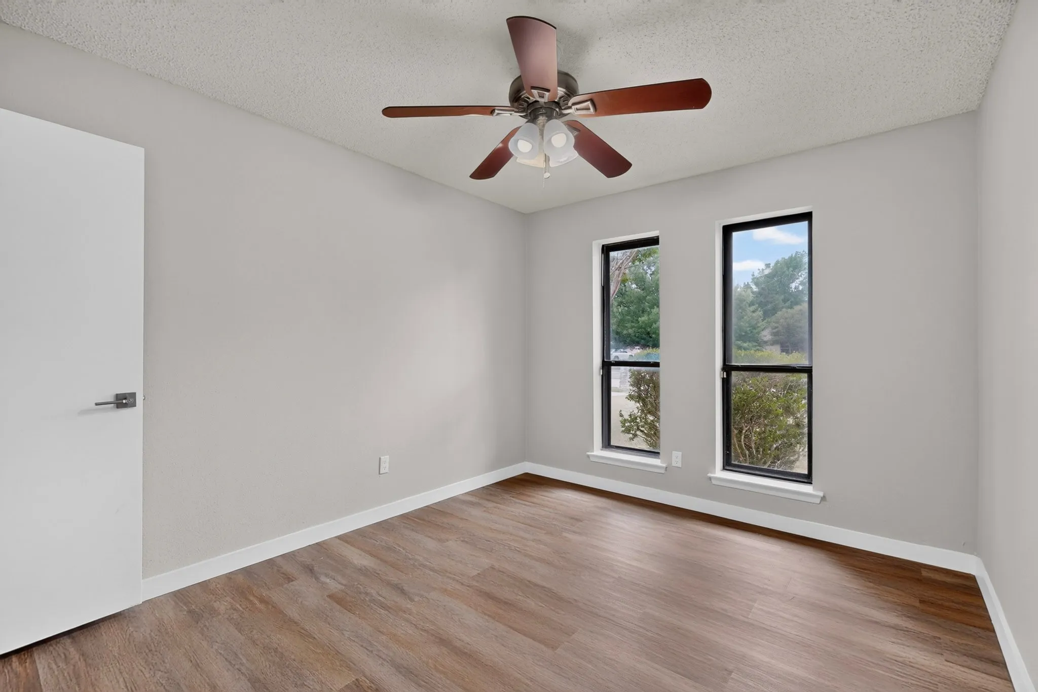Wood-finish flooring with a neutral paint palette, two large windows, and a ceiling fan with integrated lighting