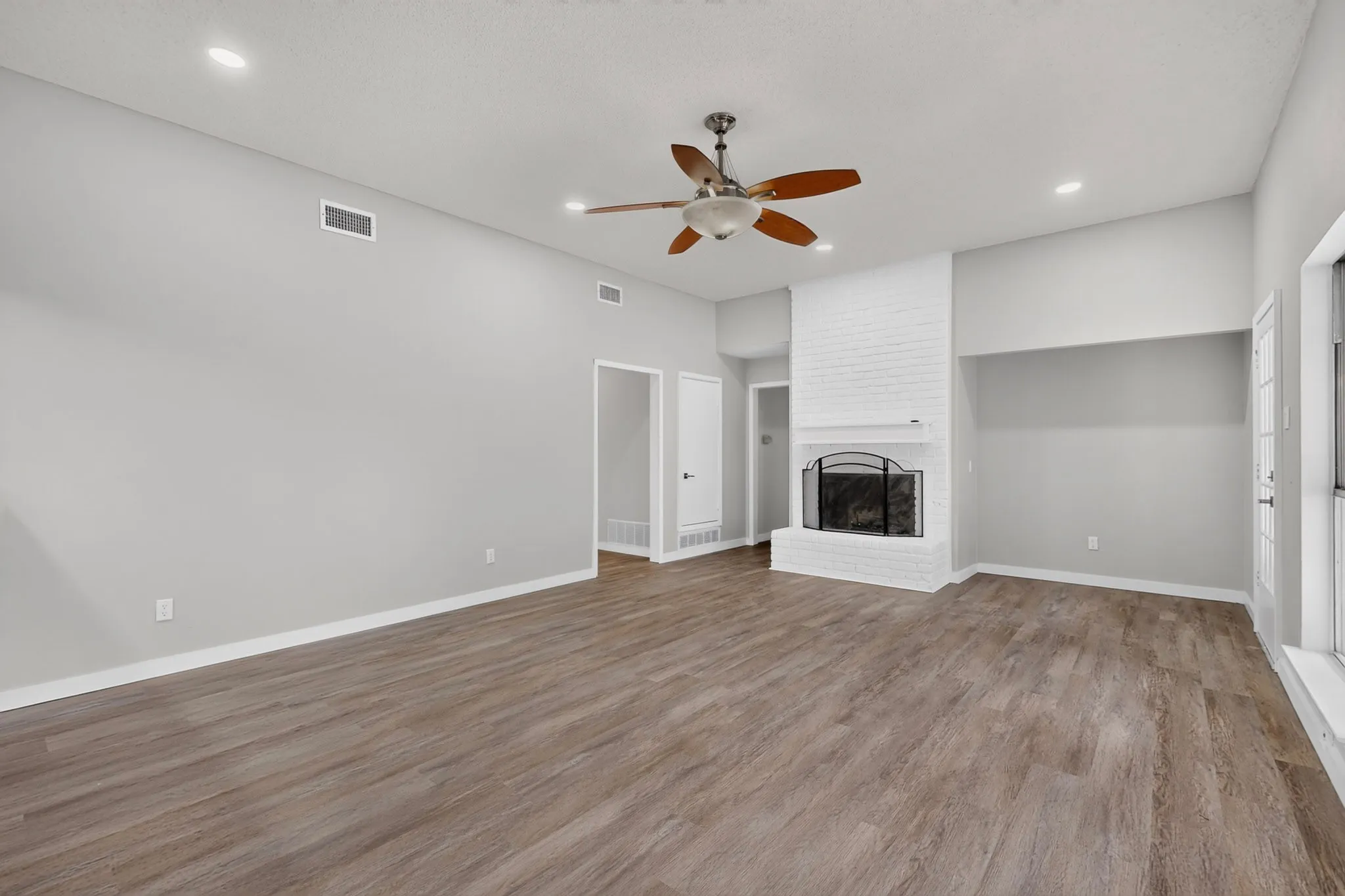 Vaulted ceiling with a ceiling fan, recessed lighting, wood-finish flooring, white brick fireplace, and a white interior door