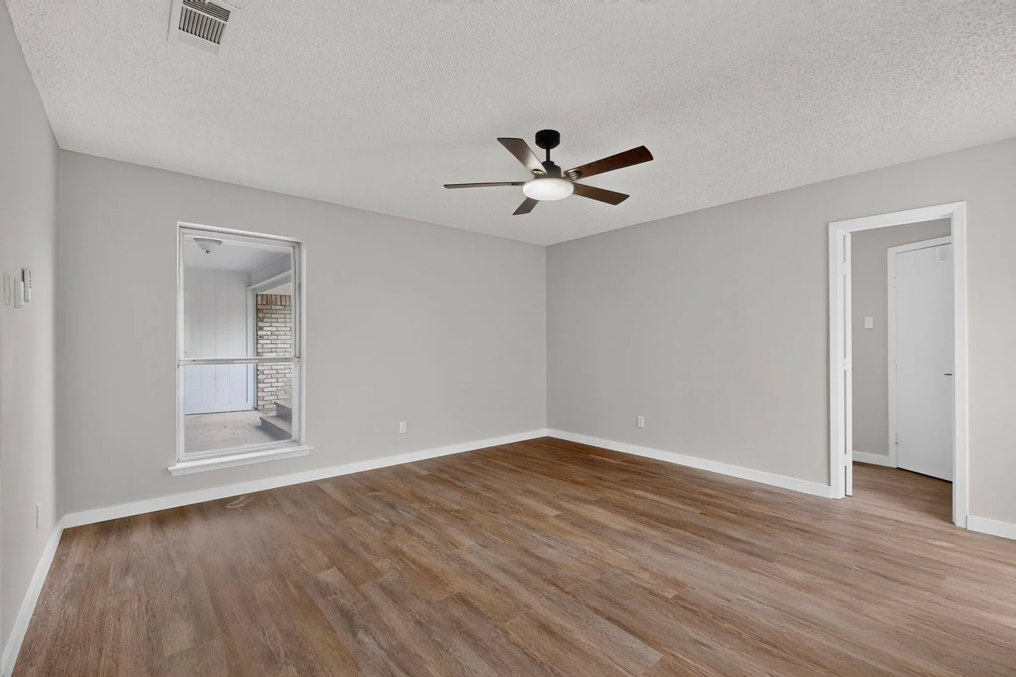 Wood-finish flooring, neutral wall tones, ceiling fan with integrated lighting, and a window with a sill