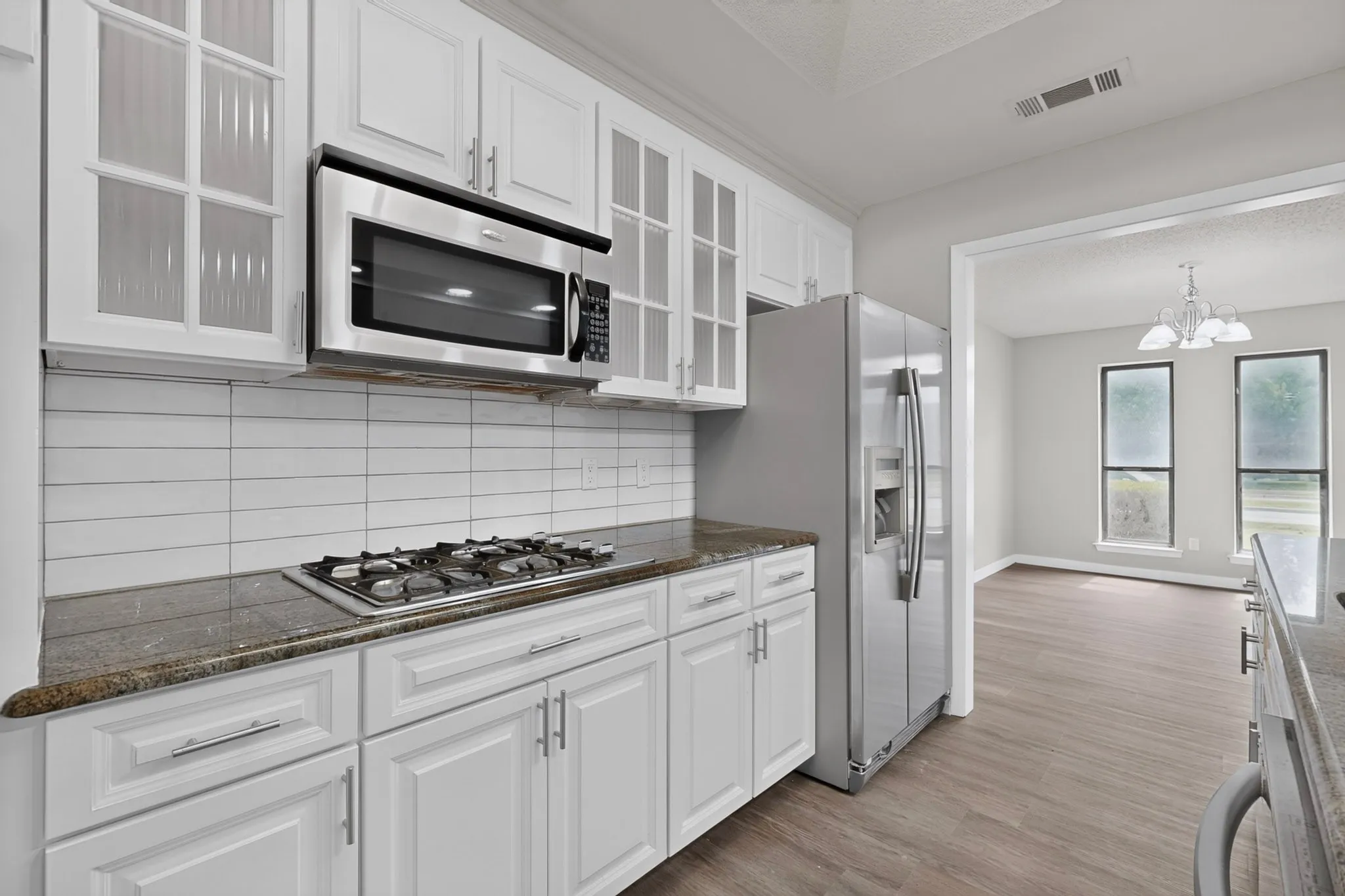 White cabinetry with brushed nickel hardware, stainless steel appliances, dark stone-finish countertops, white subway tile backsplash, and wood-finish flooring