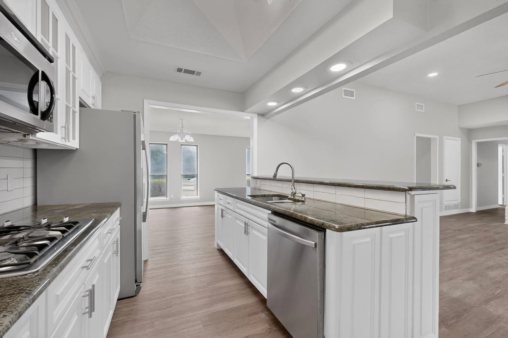 Kitchen featuring white cabinetry, stainless steel appliances, granite countertops, and wood-finish flooring