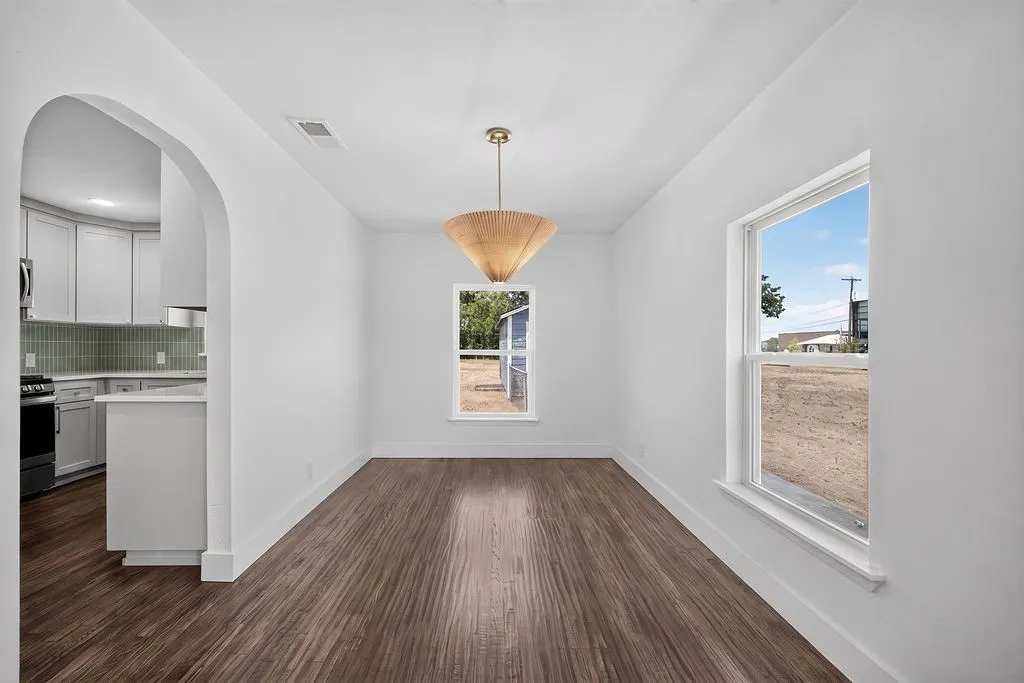 Archway opening into the kitchen, wood-finish flooring, two windows, and a decorative pendant light fixture