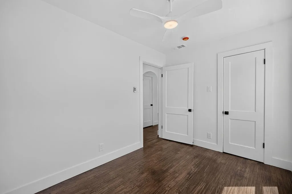Hardwood-style flooring, white walls, two-panel doors with dark hardware, and a ceiling fan with integrated lighting