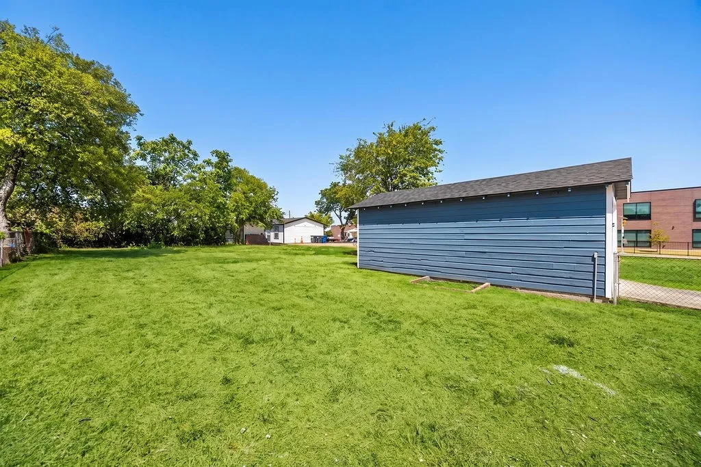 Expansive grassy lot featuring mature trees and a detached structure with blue siding and an asphalt shingle roof