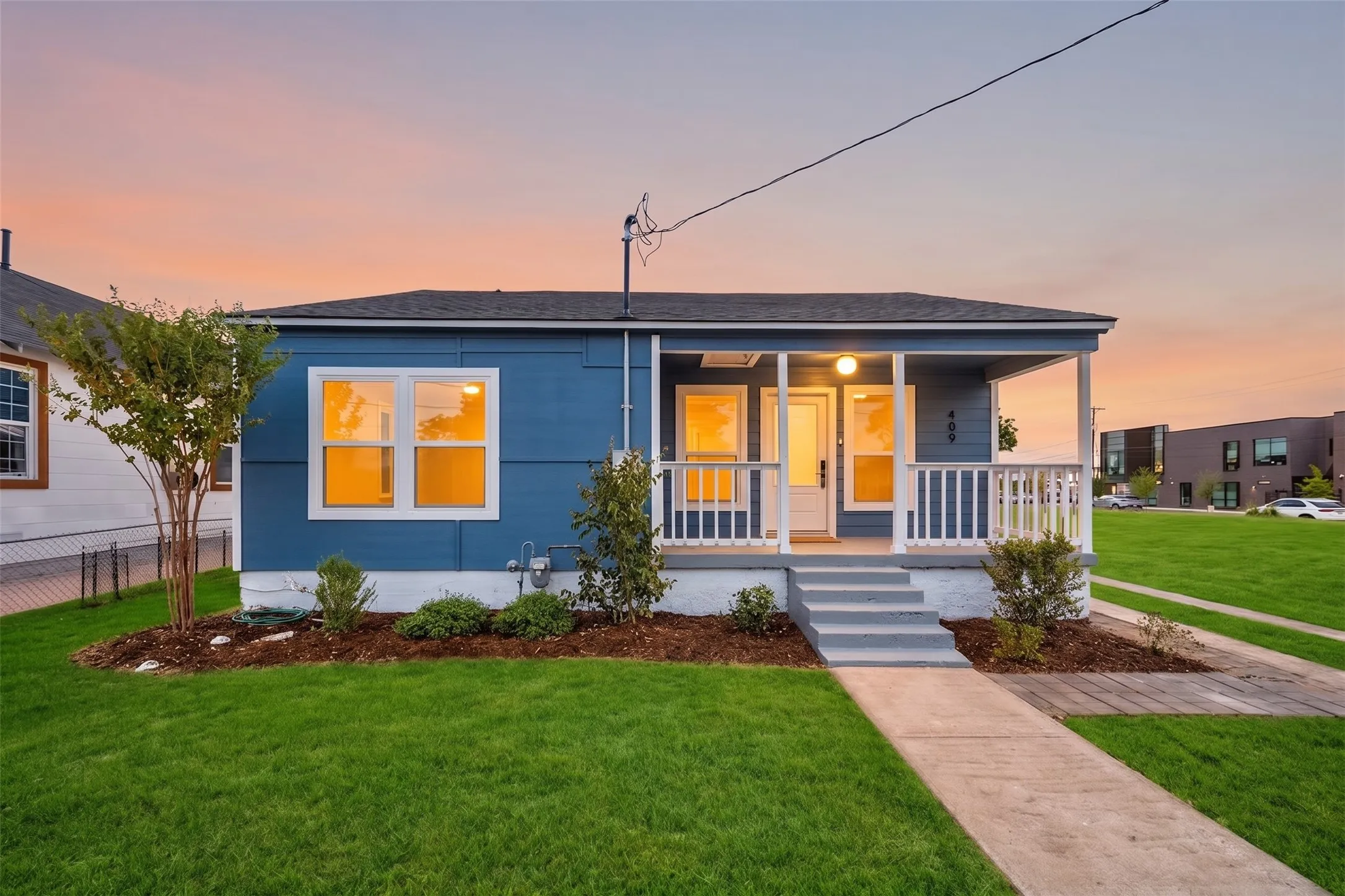 Blue exterior siding with white trim, covered front porch, concrete pathway, and front yard landscaping