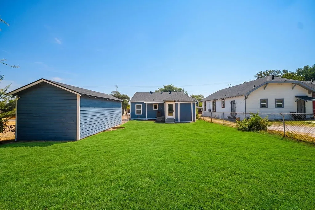 Expansive green lawn with a detached shed and additional structure, featuring chain-link fencing