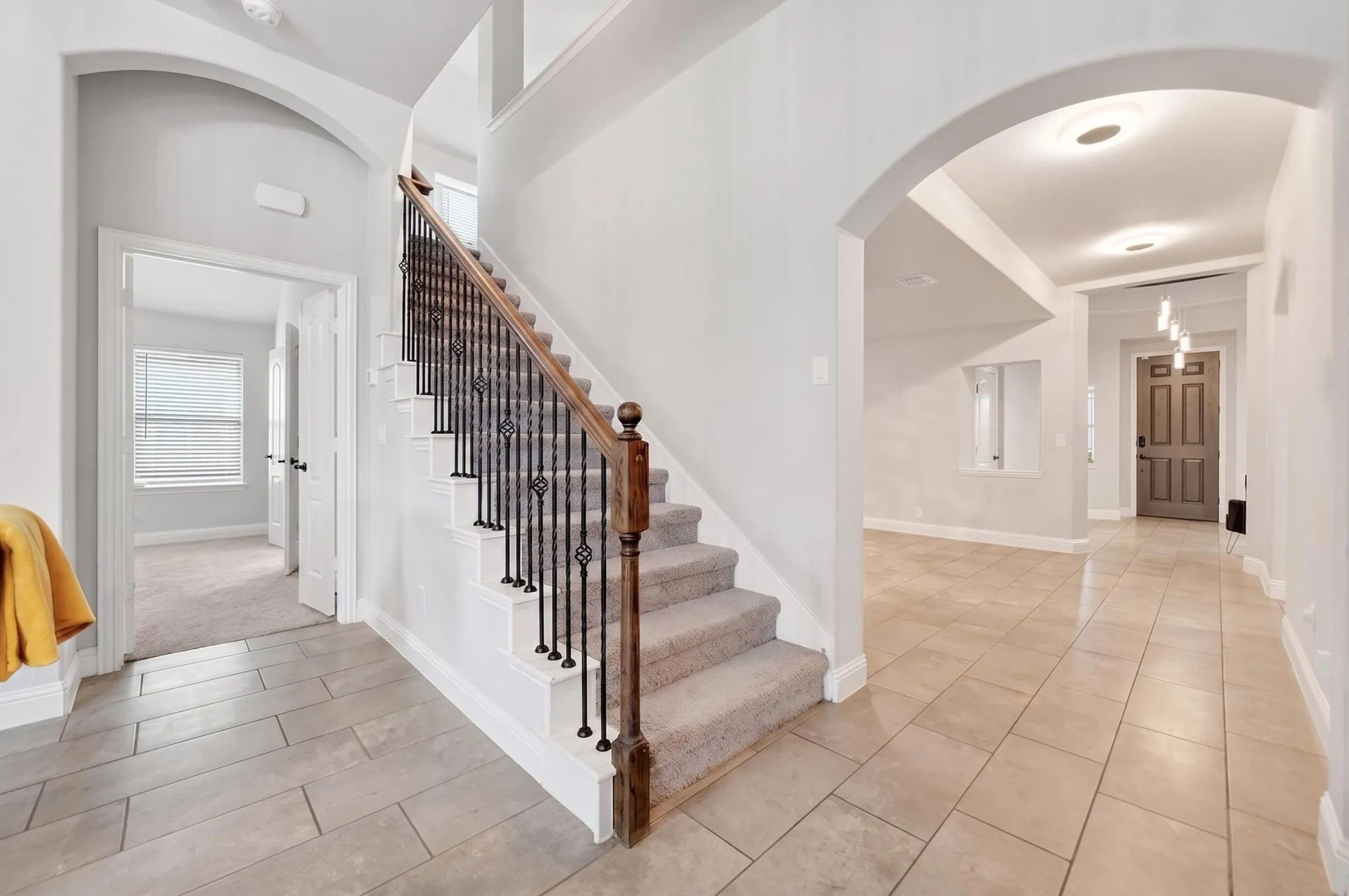 Grayscale tile flooring, carpeted staircase with wrought iron balusters, wood handrail, arched doorways, and recessed lighting