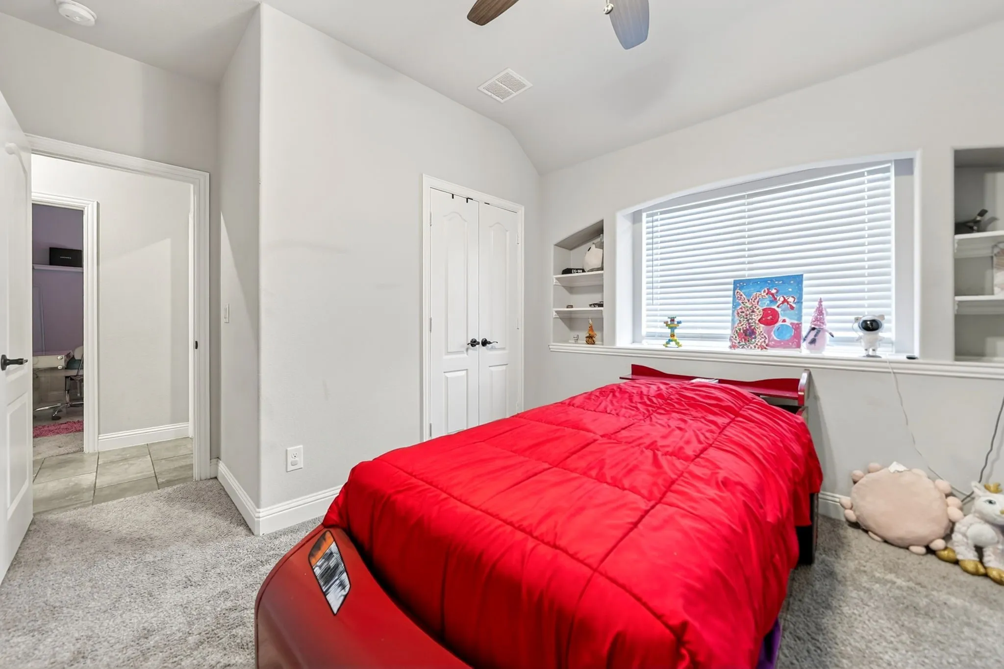 Carpeted room with a ceiling fan, arched window, and built-in shelving