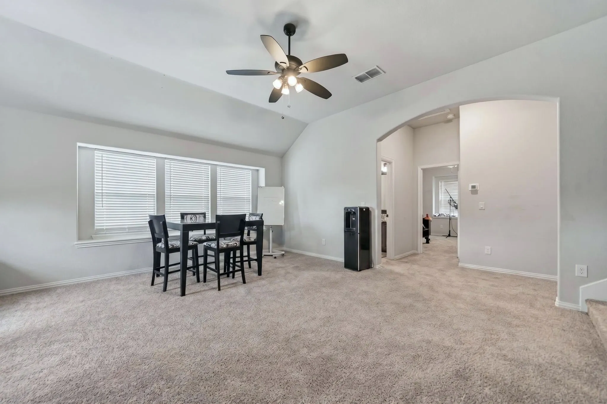 Vaulted ceiling with a ceiling fan, light gray wall paint, light-colored carpeting, multiple windows with blinds, and an arched entryway