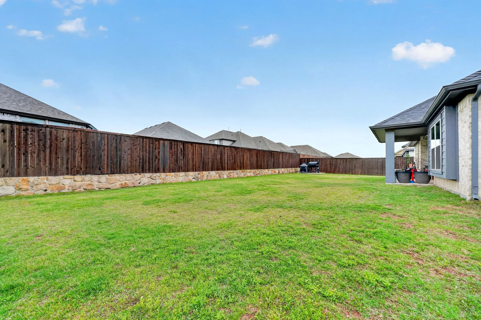 Spacious backyard featuring a manicured lawn, a wood privacy fence with a stone base, and a covered patio area