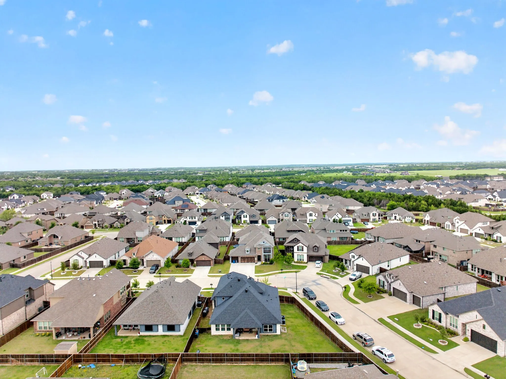Aerial perspective of a developed residential community featuring a variety of single-family homes with diverse architectural styles, asphalt shingle roofs, and paved driveways