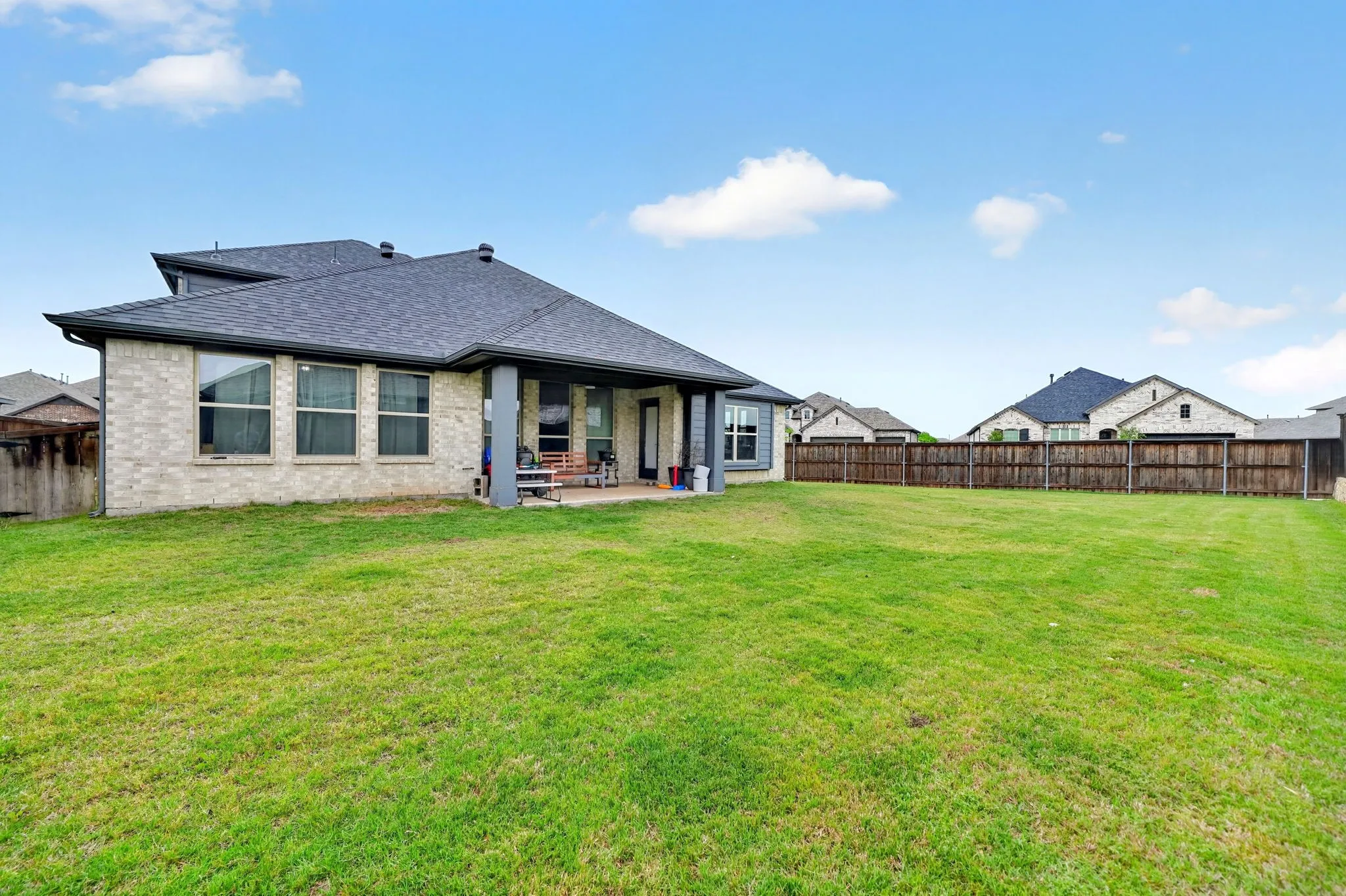 Expansive backyard featuring a manicured lawn, full privacy fencing, and a covered patio with direct access to the interior