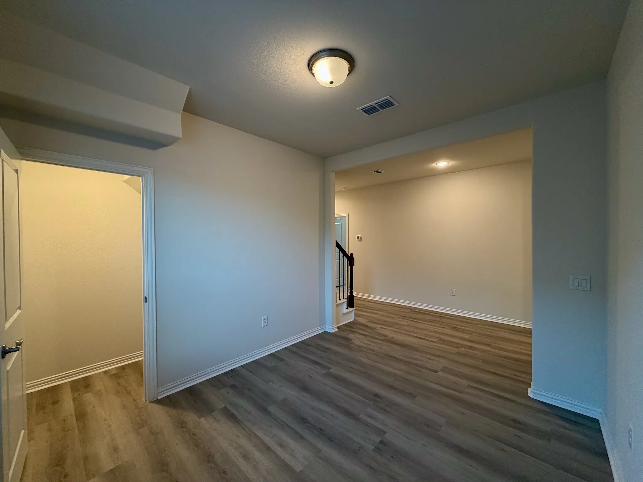 Wood-finish flooring throughout, recessed ceiling lighting, a contemporary semi-flush ceiling fixture, and a staircase with a black metal railing