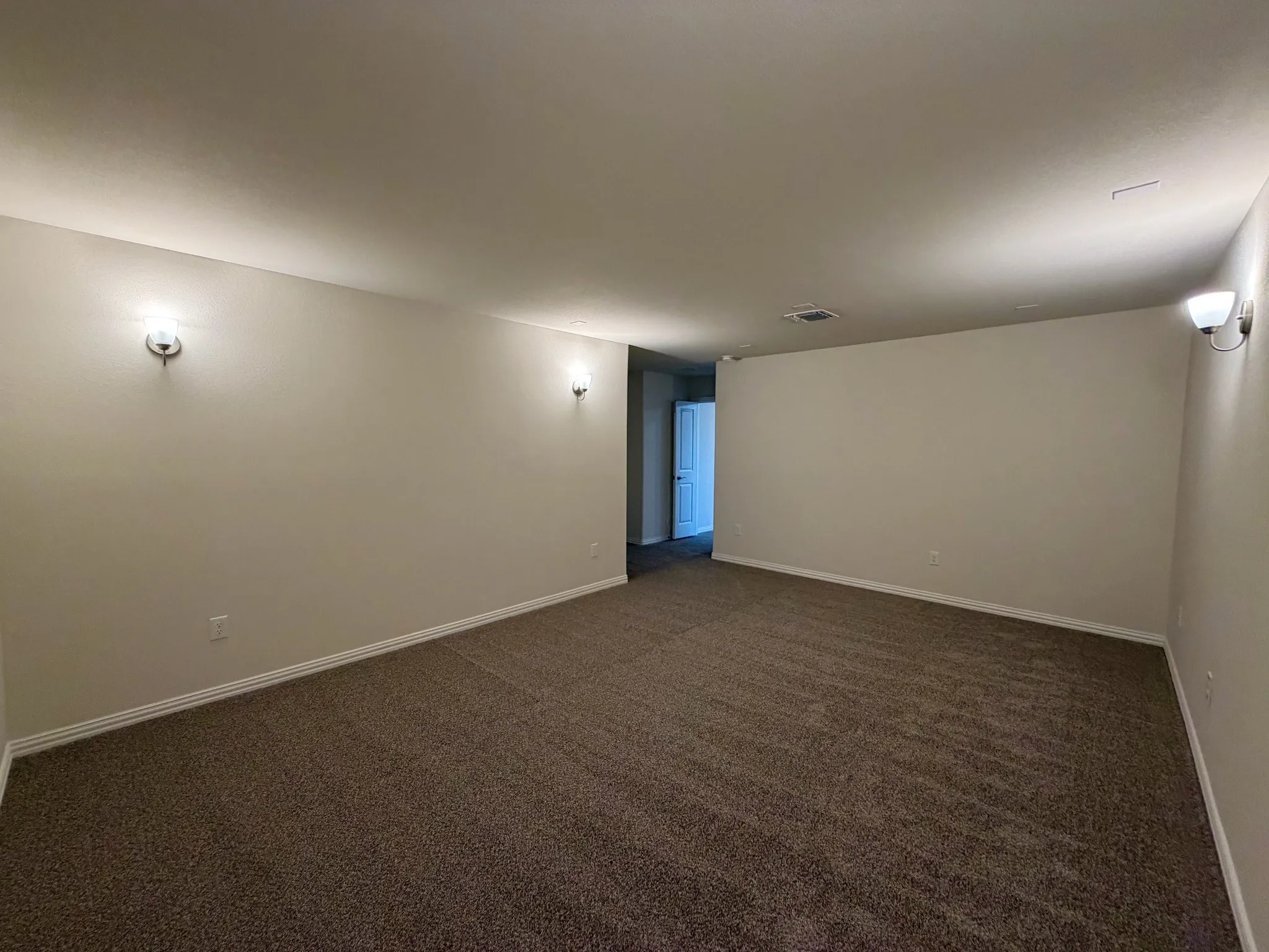 Spacious room with plush carpet flooring, light-toned wall paint, and wall-mounted sconce lighting