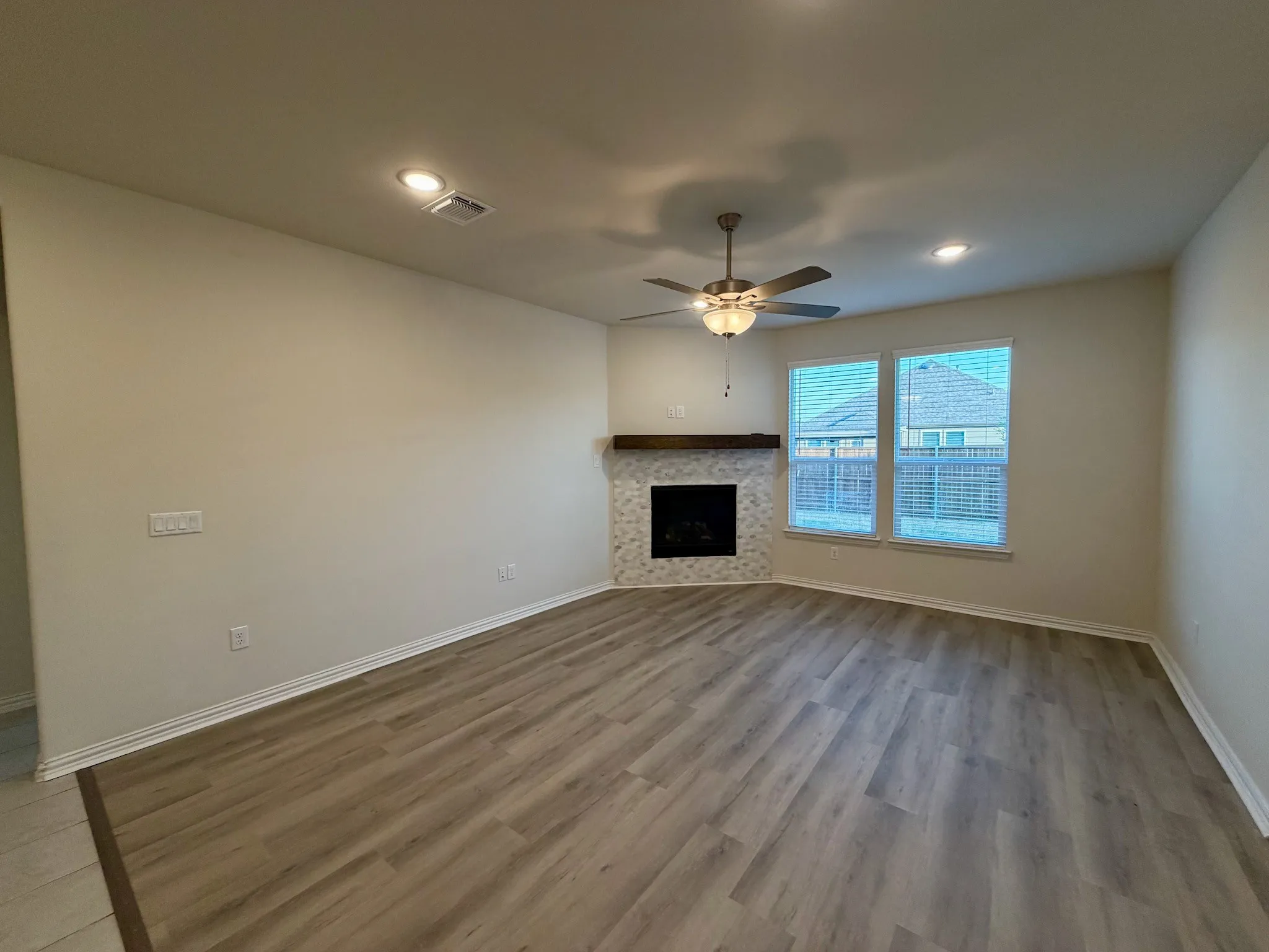 Spacious living area featuring wood-finish flooring, a tiled corner fireplace with a wood mantle, and a ceiling fan