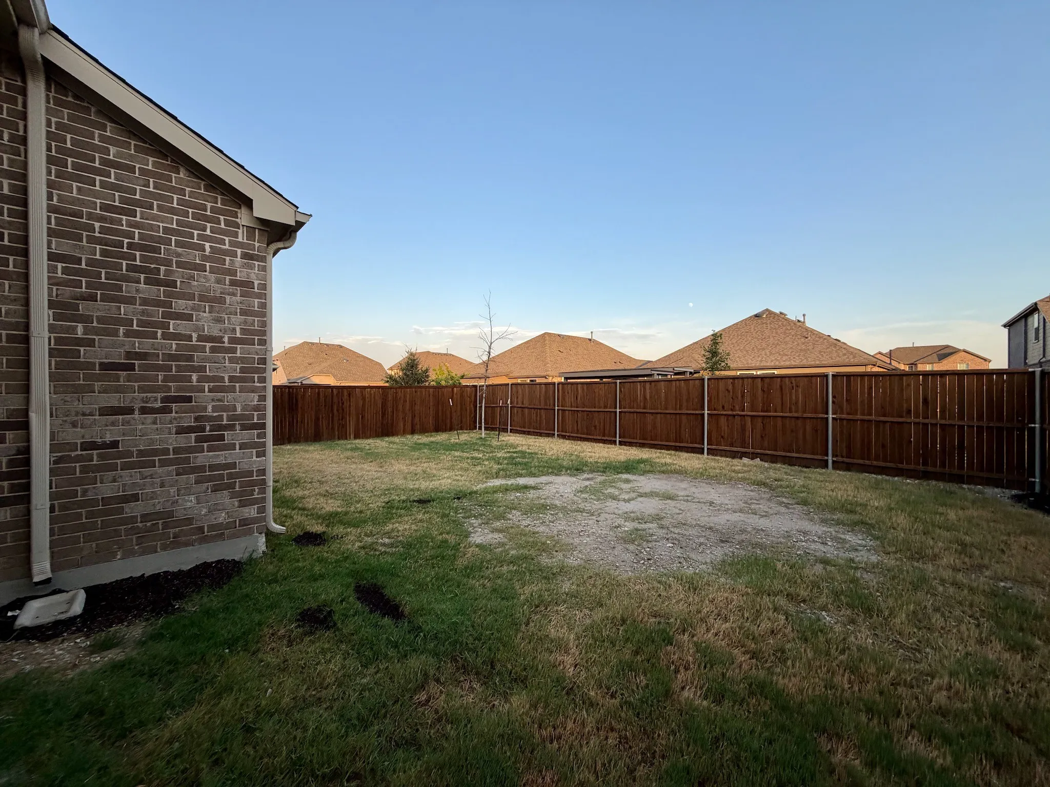 Expansive backyard featuring a stained wood privacy fence and a brick exterior