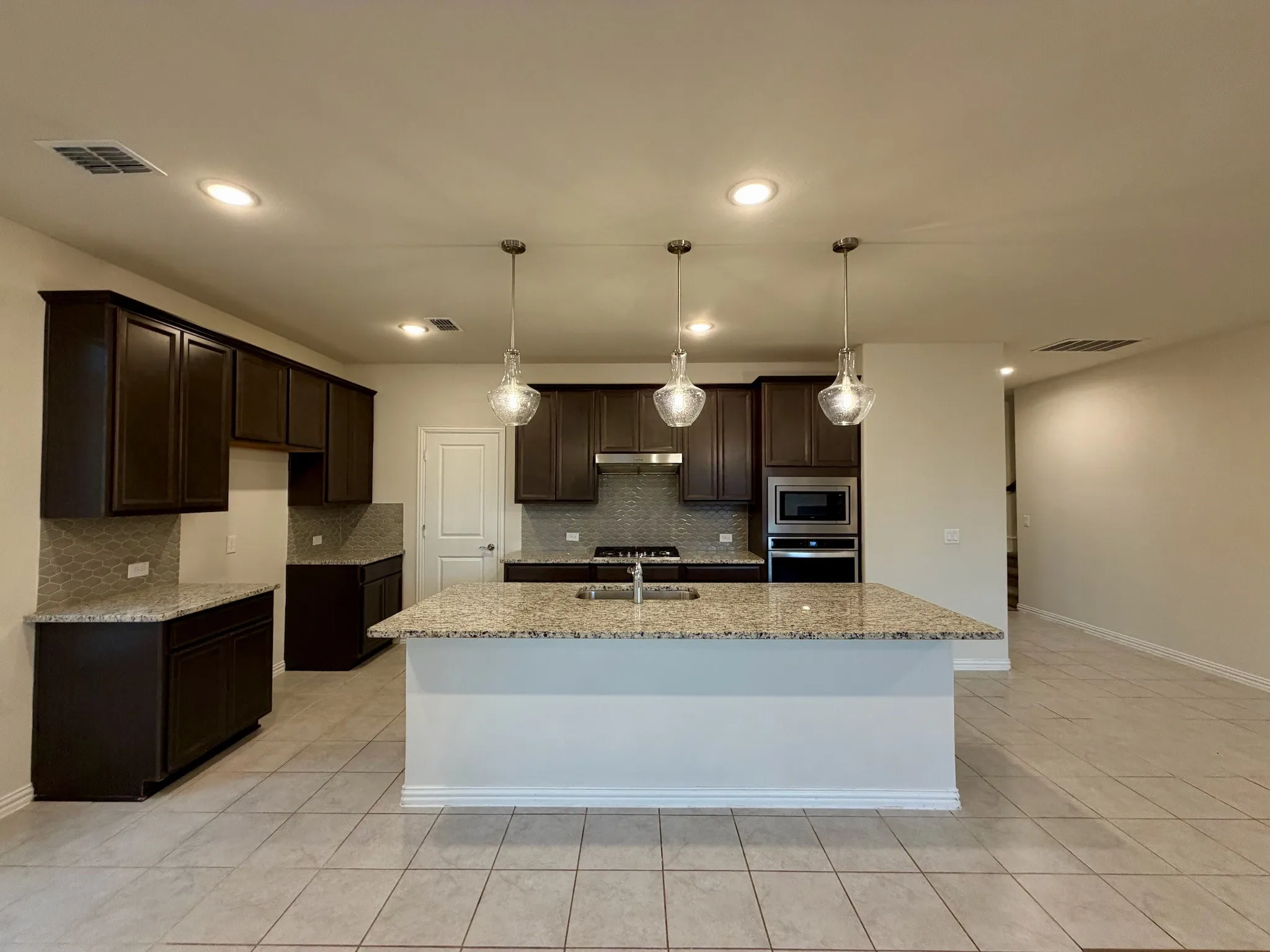 Spacious kitchen featuring an expansive island with granite countertops, dark wood cabinetry, stainless steel appliances, and tile flooring