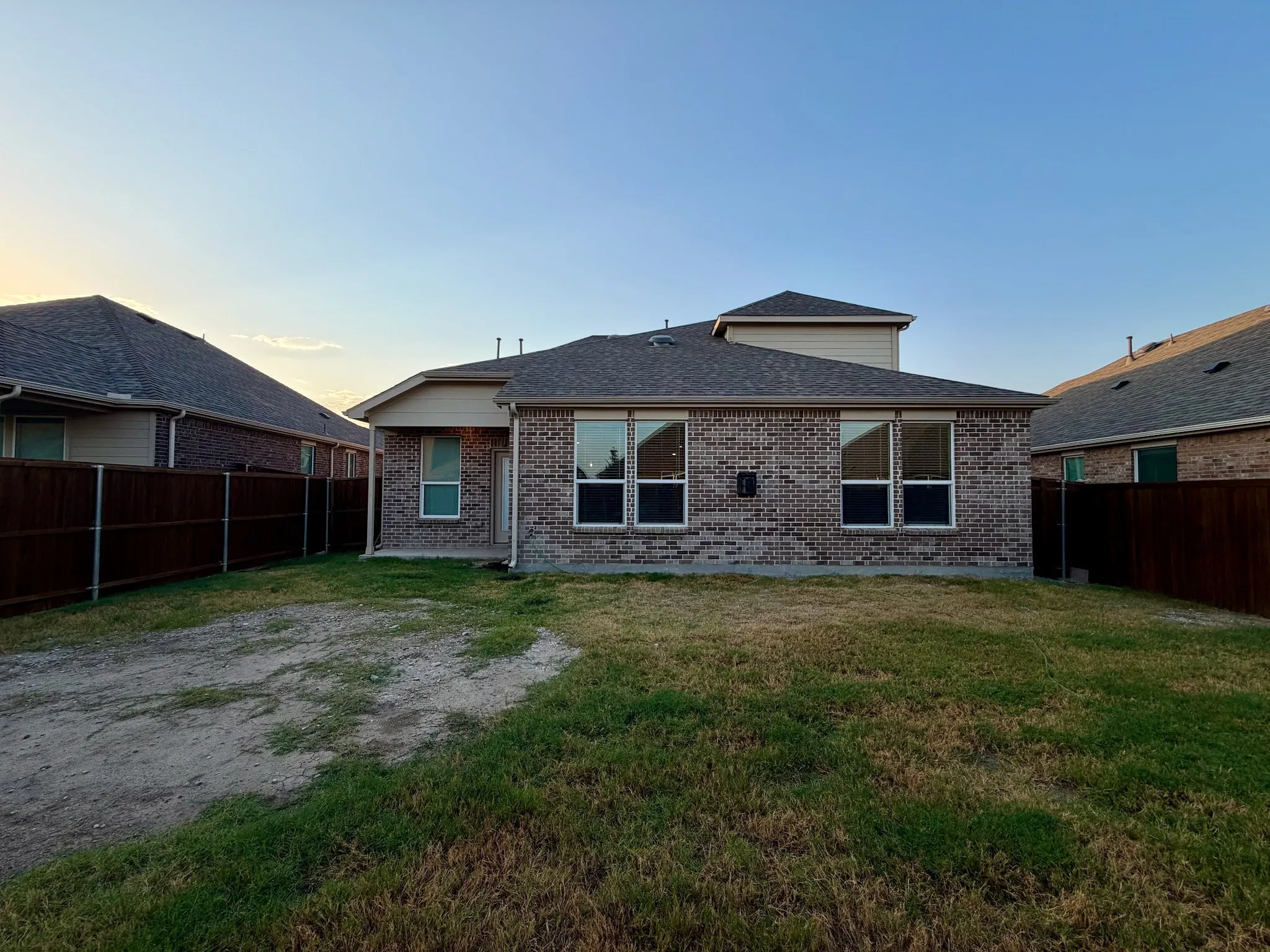 Brick exterior home featuring multiple large windows, a pitched roofline with architectural detail, and a spacious rear yard with mature landscaping and privacy fencing on both sides