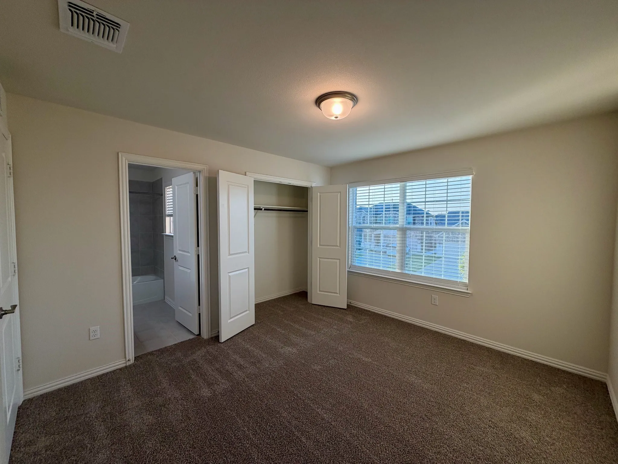 Spacious room featuring carpeted flooring, a large window with blinds, and a built-in closet with bi-fold doors