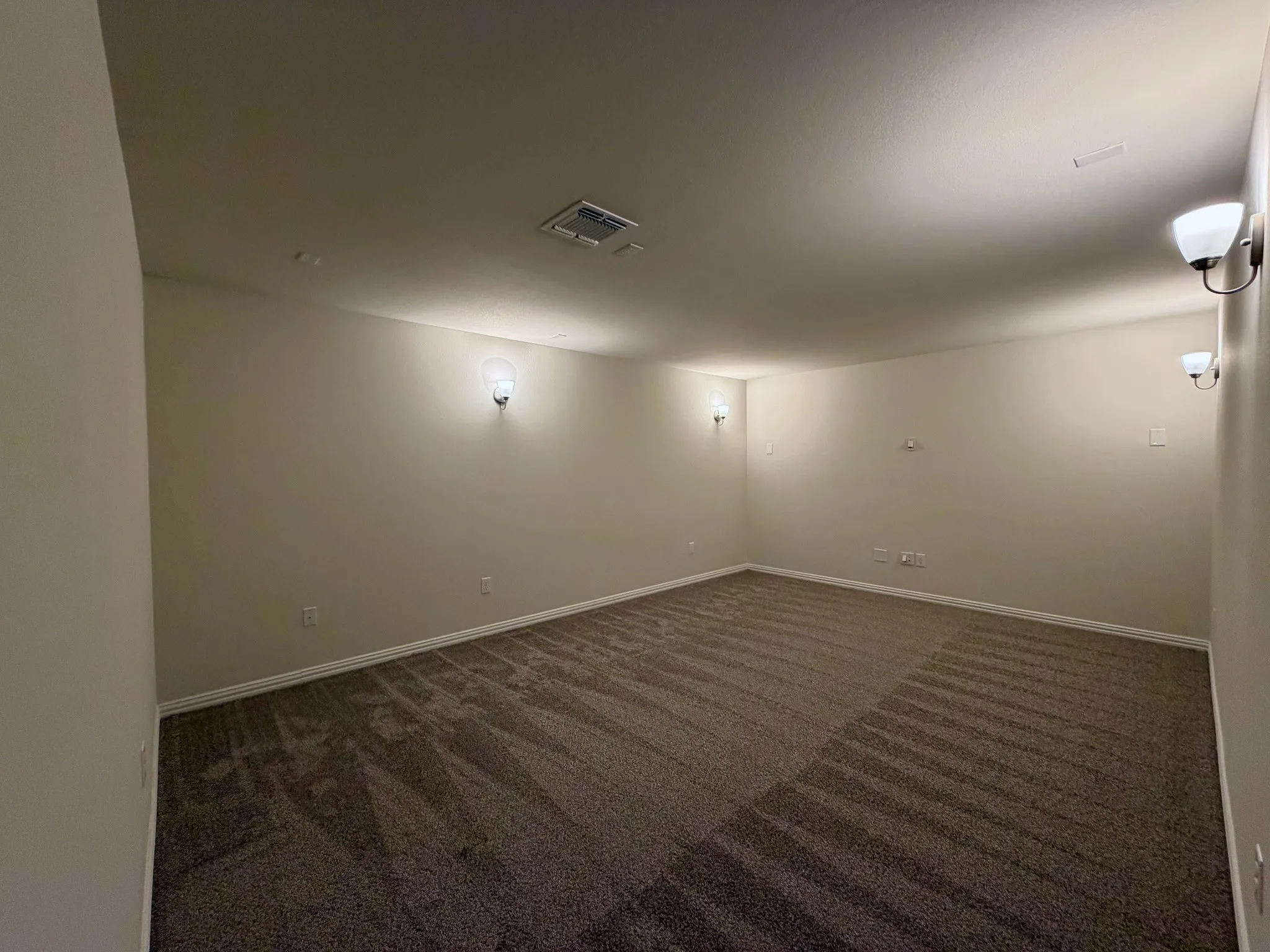 Spacious room featuring neutral carpeting, light-toned walls, and multiple wall sconces