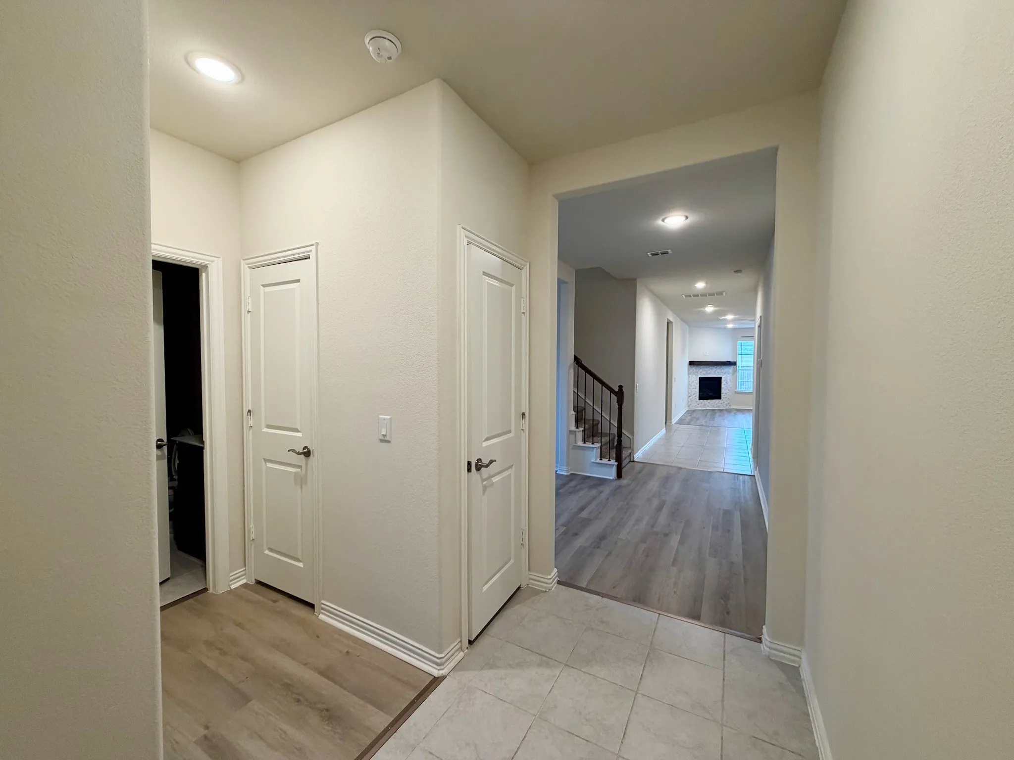 Recessed lighting illuminating the entry with tile flooring, transitioning to wood-finish flooring