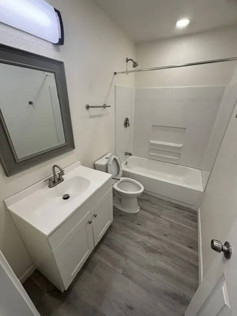 White vanity with an integrated sink, brushed nickel faucet, a framed mirror, and wood-finish flooring