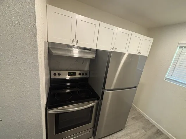 Stainless steel range, coordinating stainless steel refrigerator, white shaker-style cabinetry, and wood-finish flooring