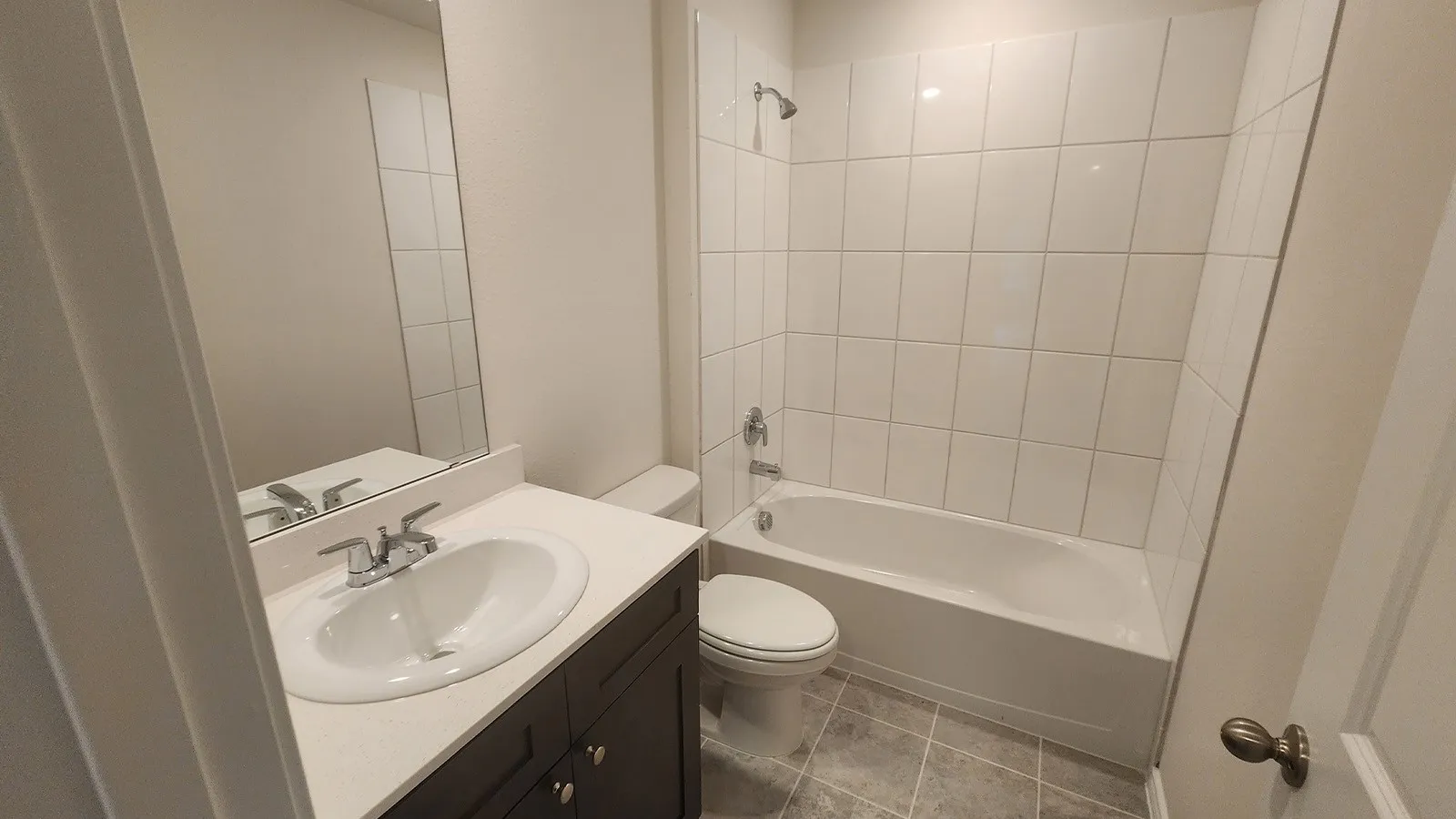 Bathroom featuring a white subway tile shower surround, a white bathtub, a dark wood-finish vanity with a white countertop, and a vanity mirror