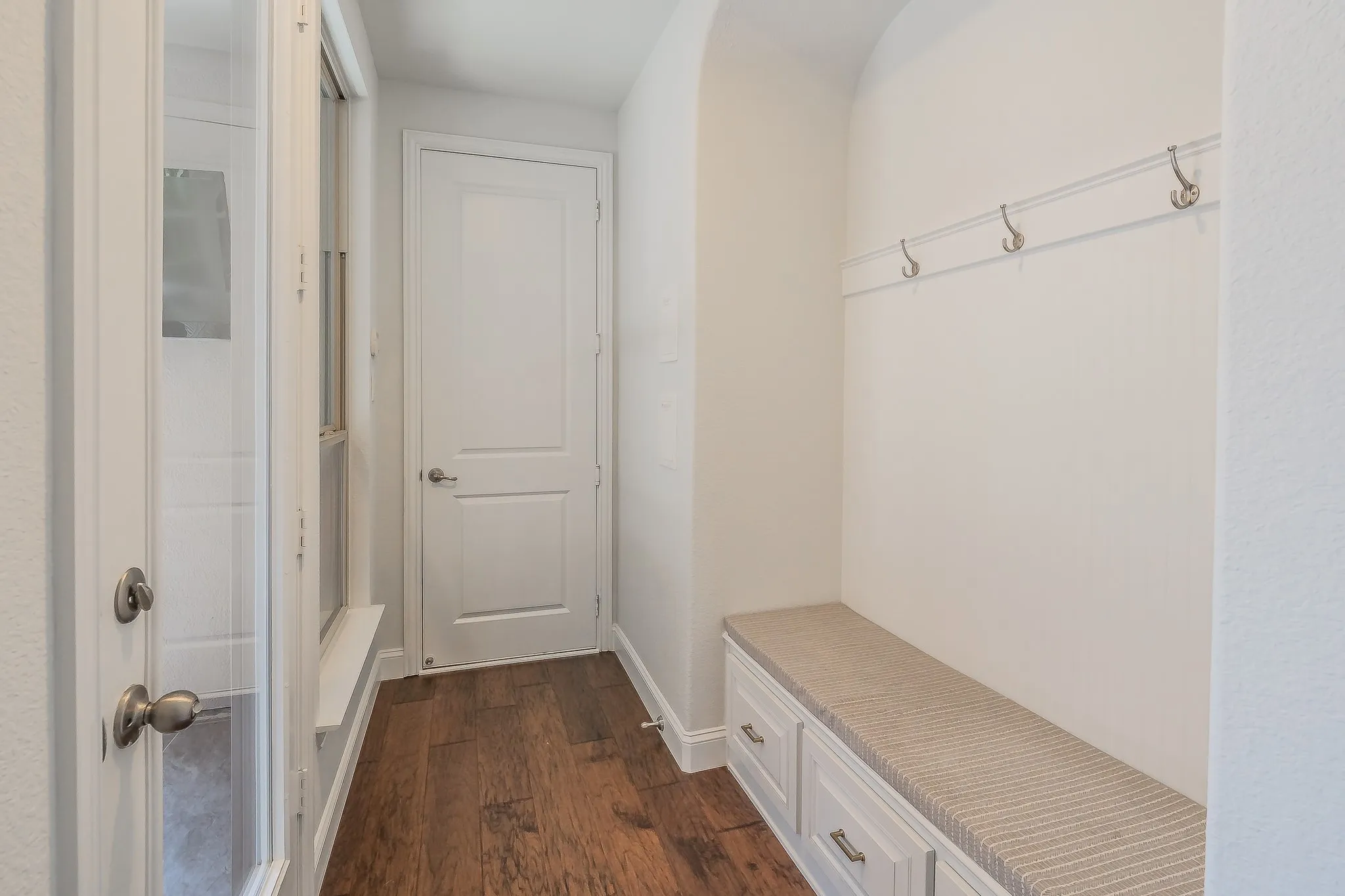 Entryway featuring wood-finish flooring, built-in bench with storage, wall-mounted coat hooks, and paneled doors