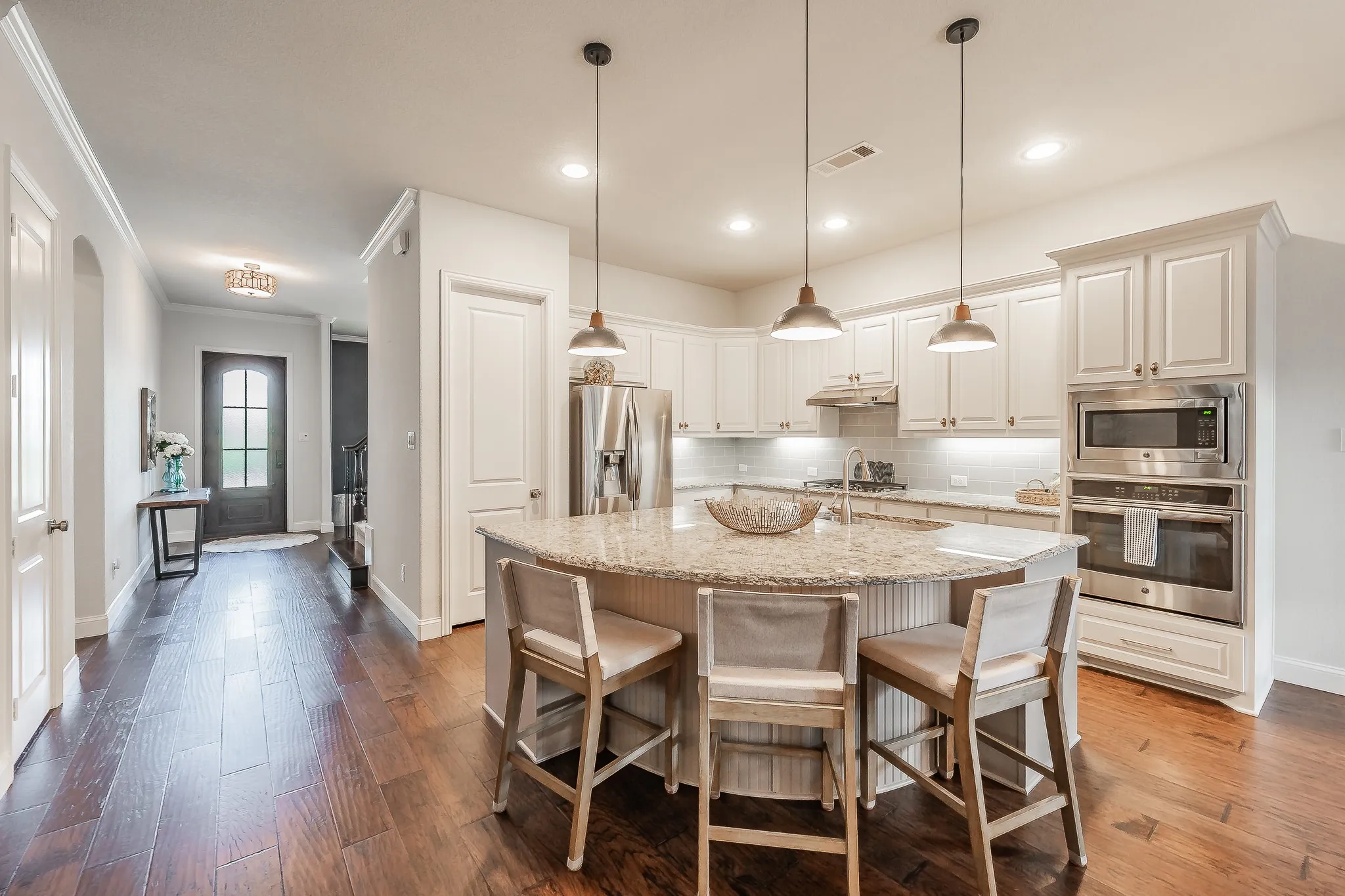 Gourmet kitchen with white cabinetry, stainless steel appliances, a large island with seating, and pendant lighting