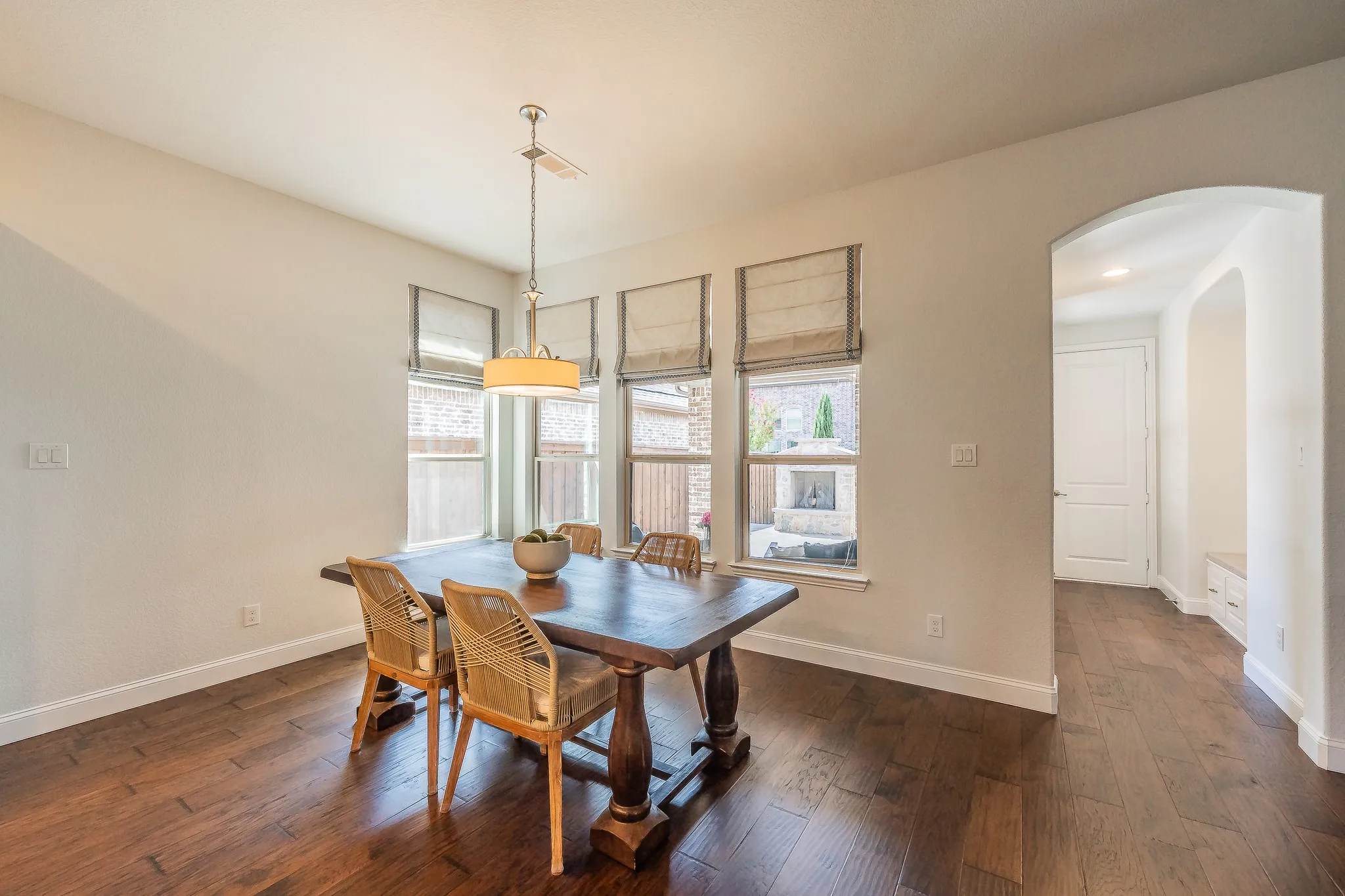 Hardwood flooring throughout, multiple windows with neutral window treatments, a ceiling-mounted light fixture, and an arched entryway