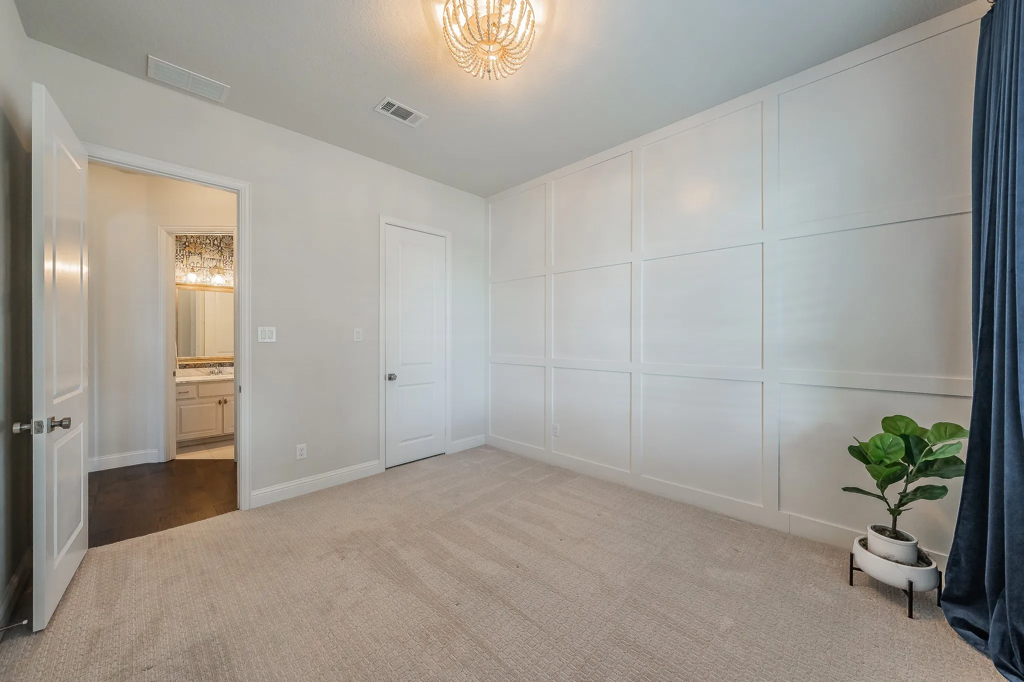 Carpeted room featuring a decorative panel accent wall and a chandelier-style light fixture