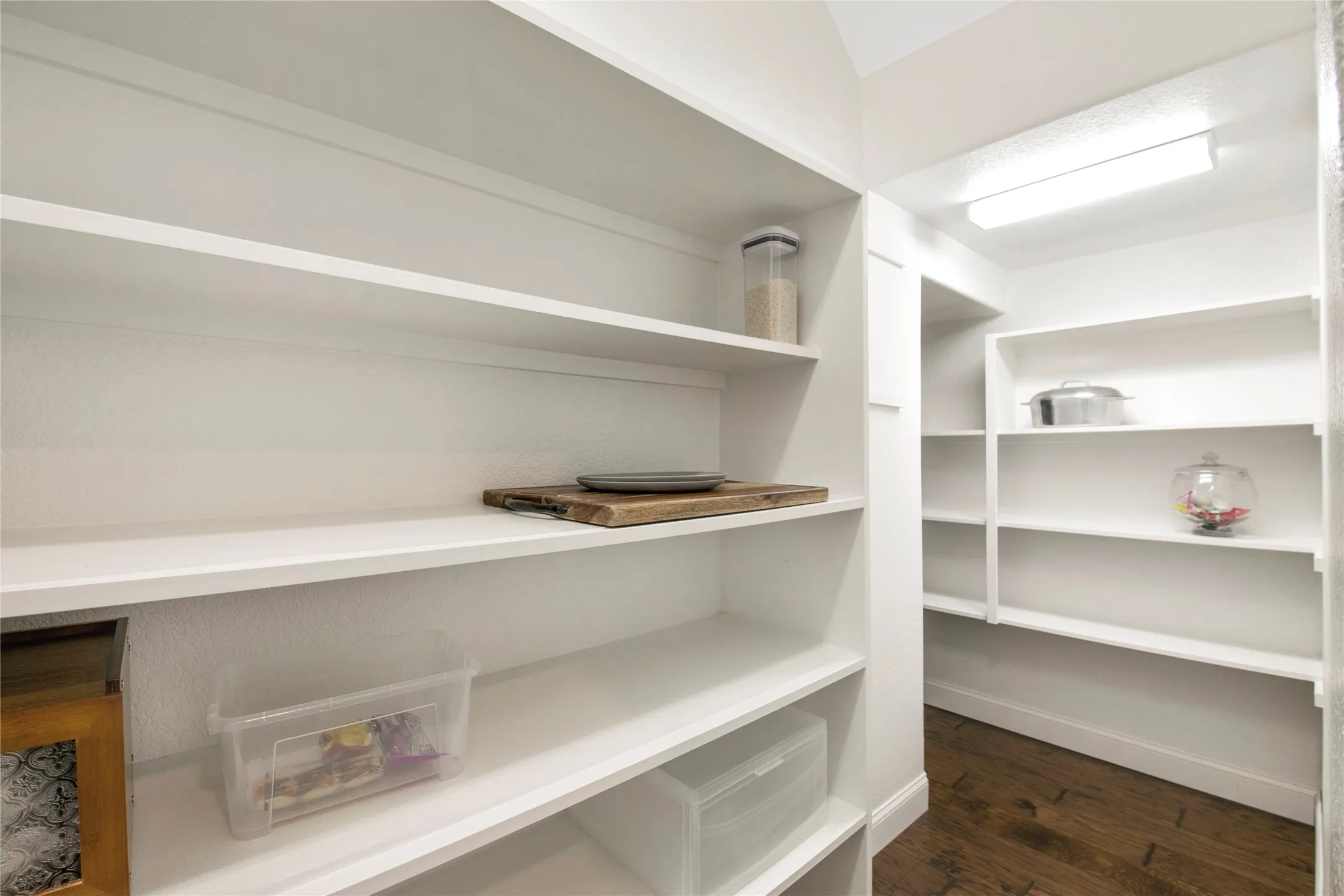 Walk-in pantry with extensive shelving, white painted walls, and wood-finish flooring