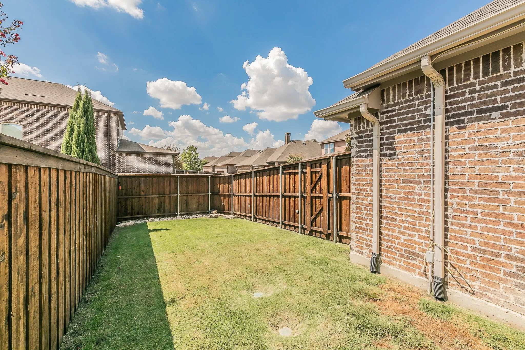 Expansive backyard featuring a manicured lawn, full privacy fencing, and brick exterior