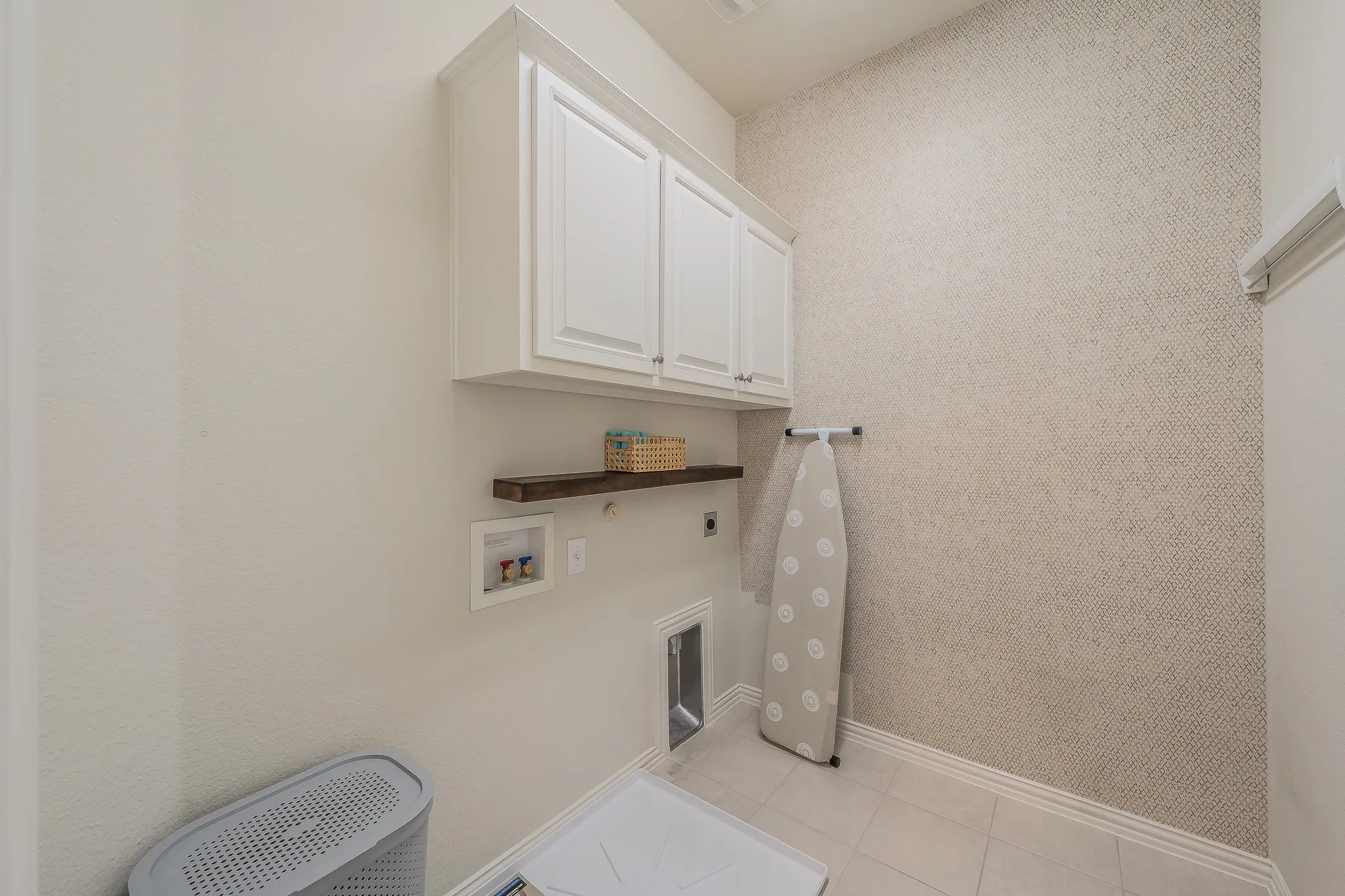 White cabinetry, wood-finish shelving, textured accent wall, tile flooring, and utility hookups