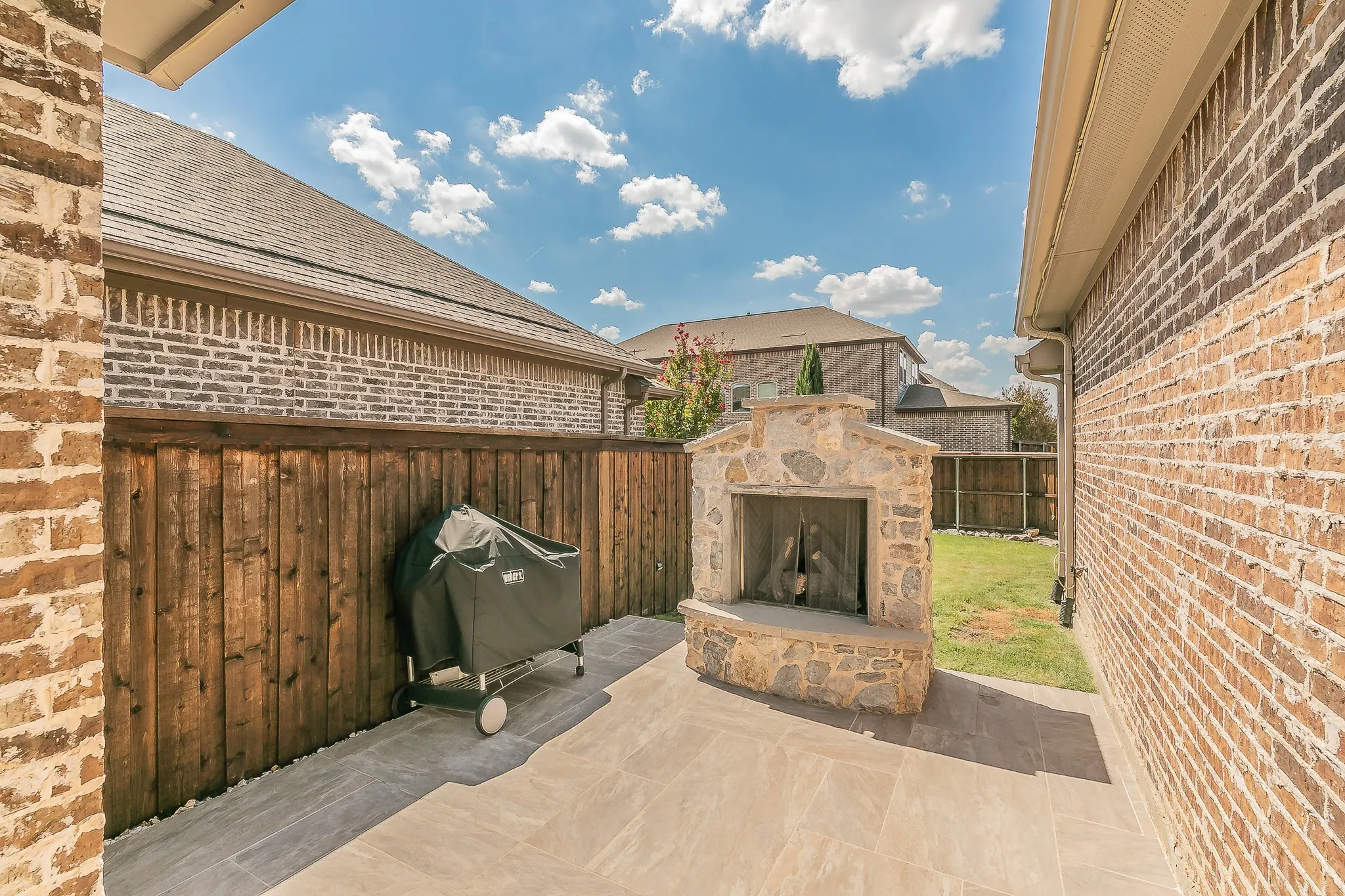 Outdoor patio featuring a stone-clad fireplace, tile flooring, and a wood privacy fence