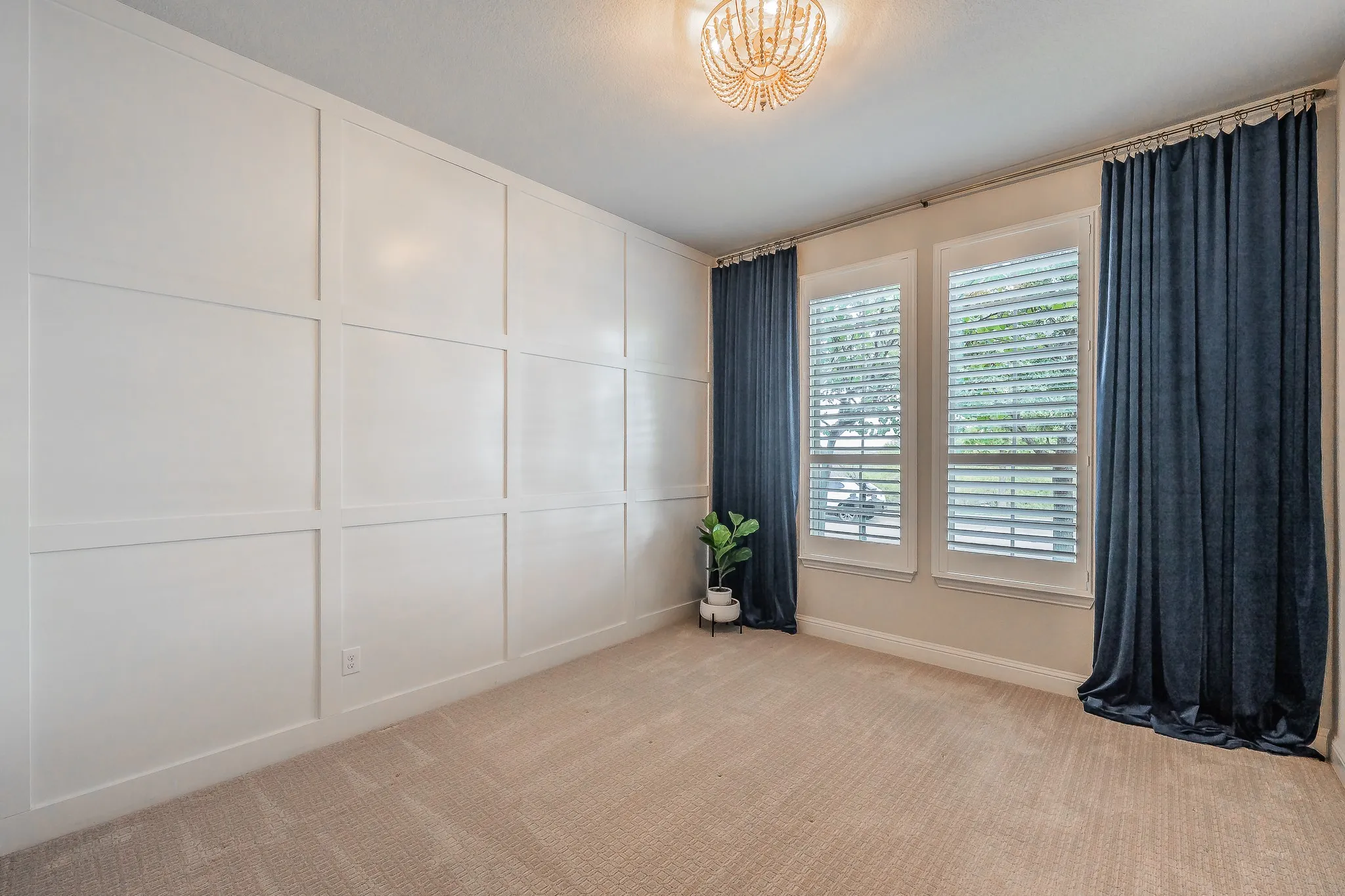 Board and batten wall accent with a bead-strand chandelier, two windows with plantation shutters, and soft carpeting