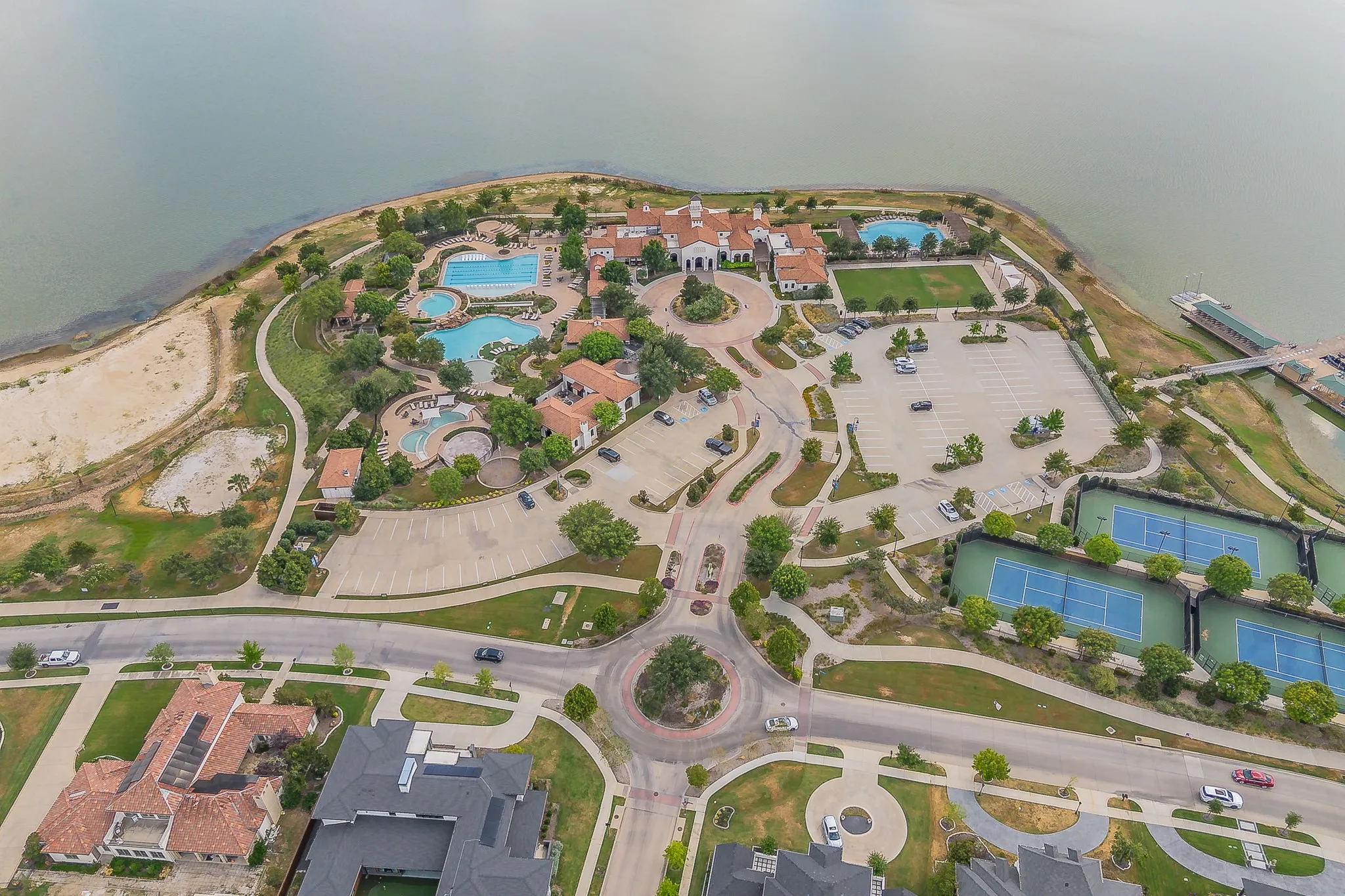 Waterfront property featuring multiple swimming pools, tennis courts, a private dock, and manicured landscaping