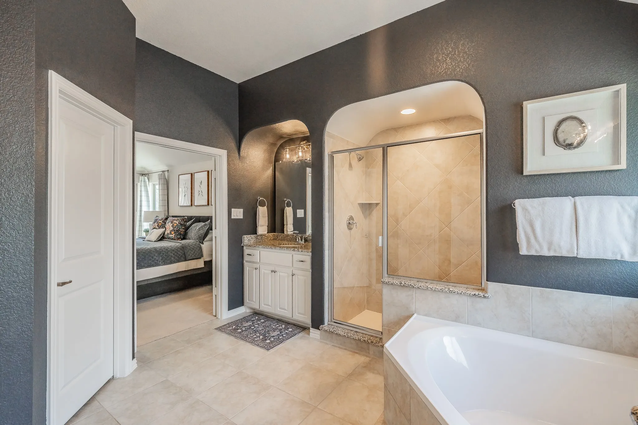 Archway entry shower with glass enclosure, separate soaking tub, single vanity with light-tone countertop, and tile flooring