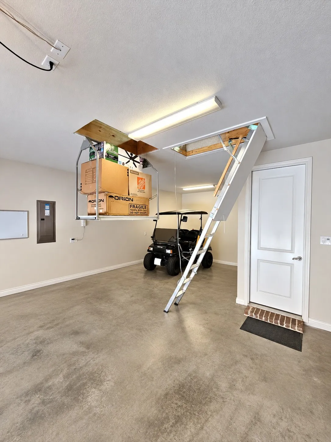 Garage space featuring a concrete floor, overhead fluorescent lighting, and an attic access ladder