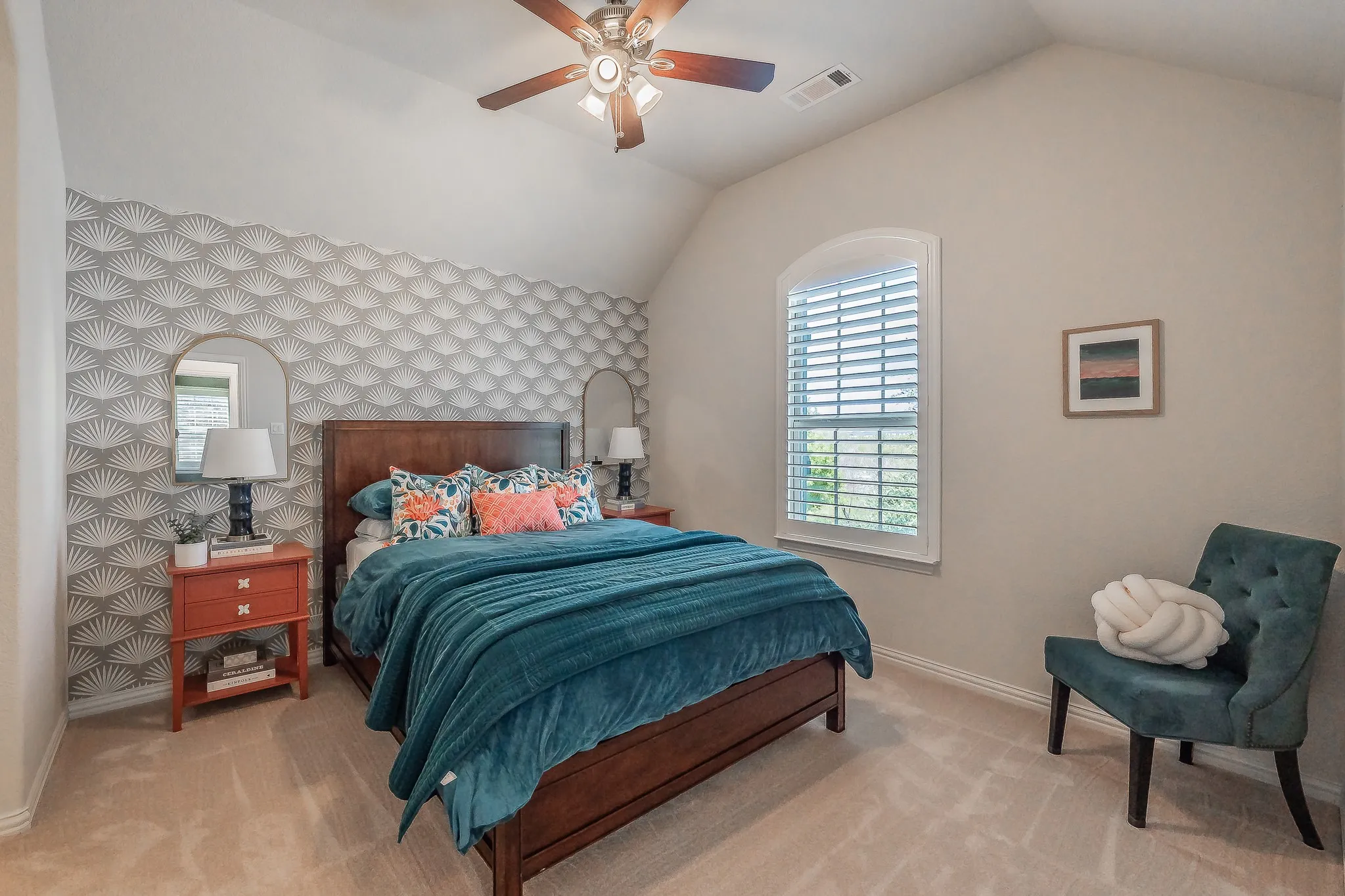 Vaulted ceiling with a ceiling fan, wall-mounted light fixtures, arched window with plantation shutters, and textured accent wall