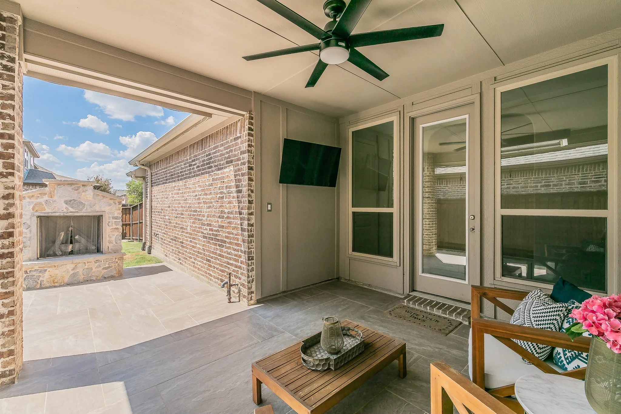 Covered patio featuring an outdoor stone fireplace, ceiling fan, and tiled flooring